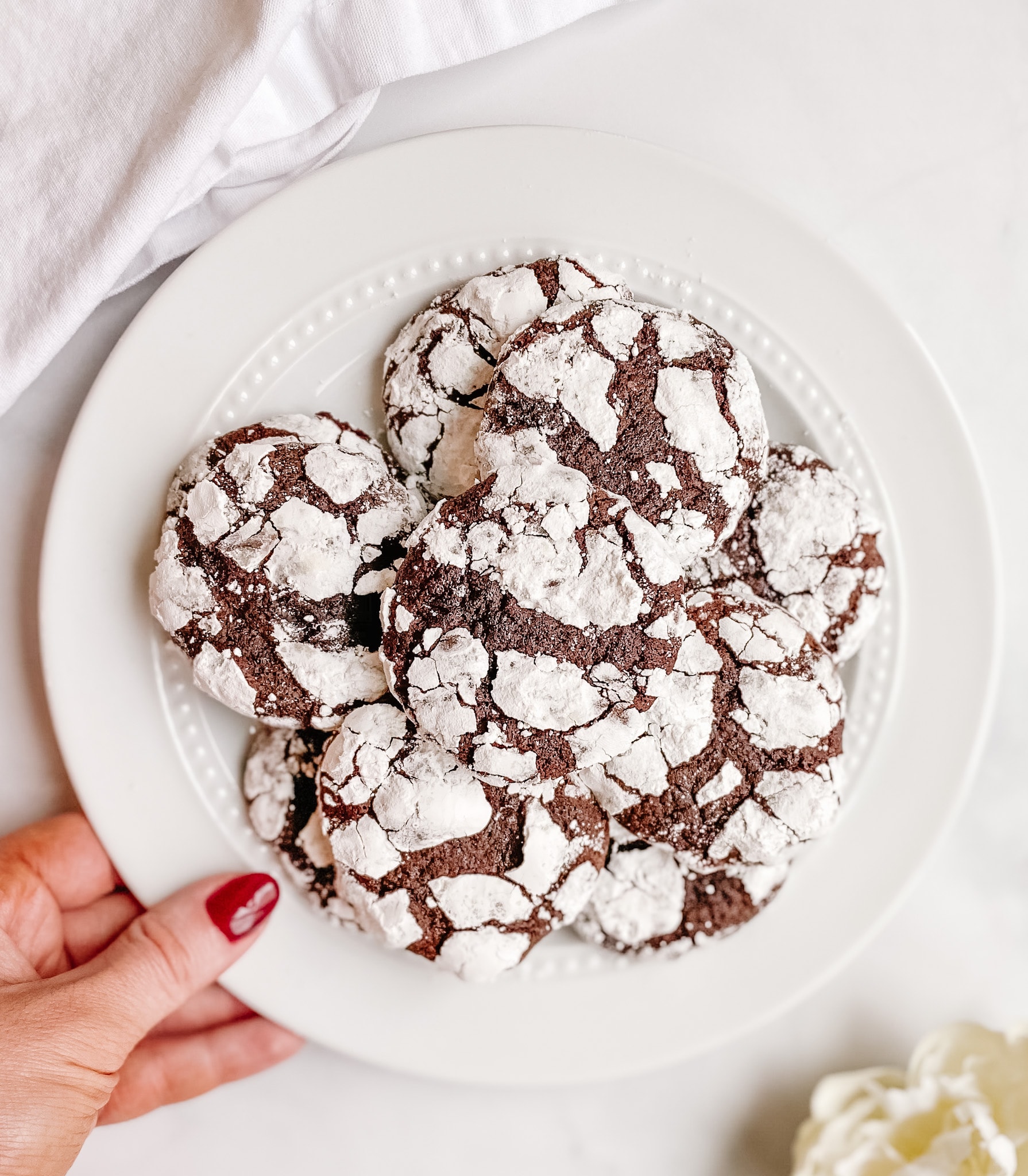 A plate of chocolate crinkle cookies being held up by a hand with bright red nails.