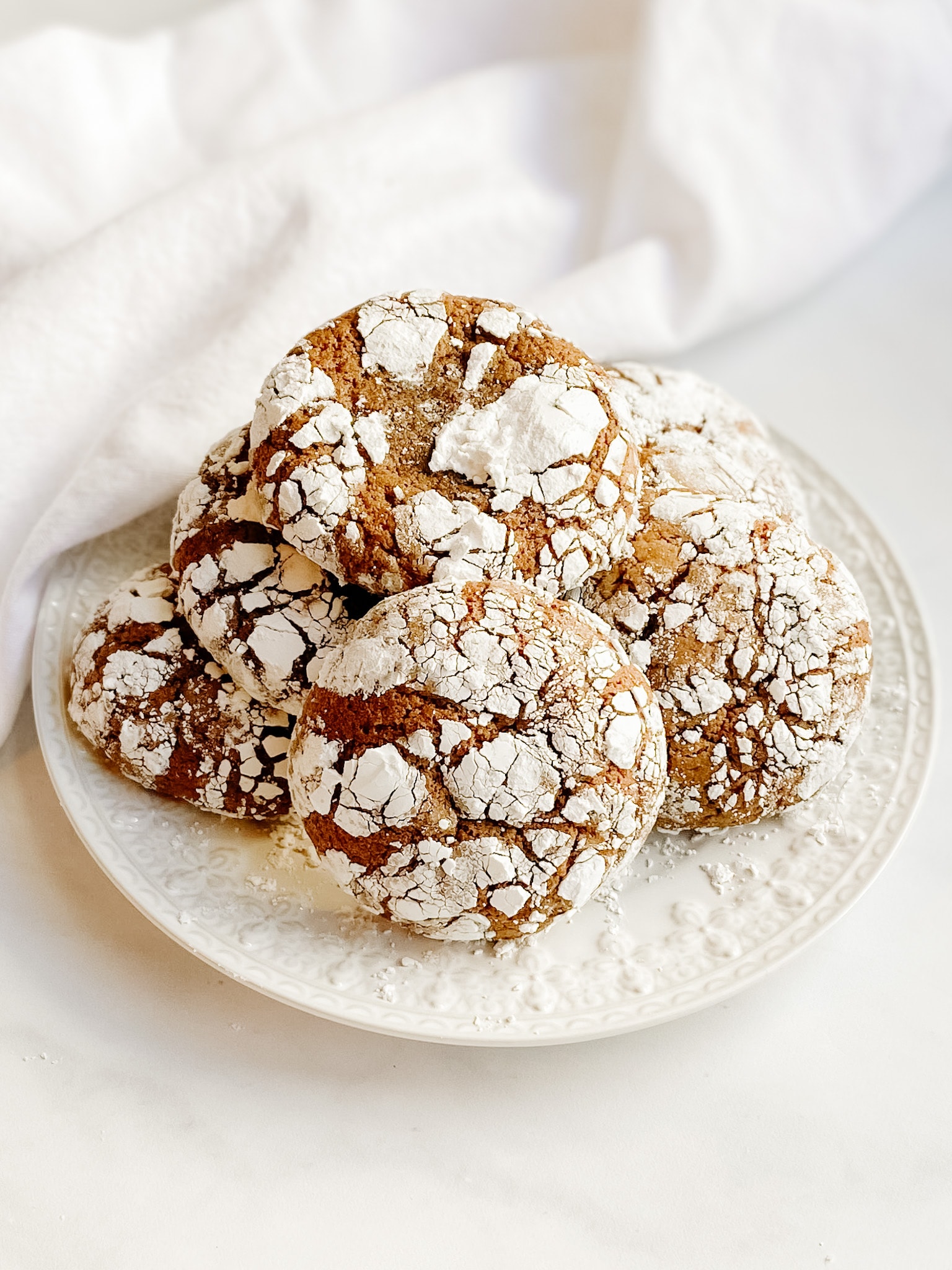 A stack of gingerbread crinkle cookies on a white decorative plate.