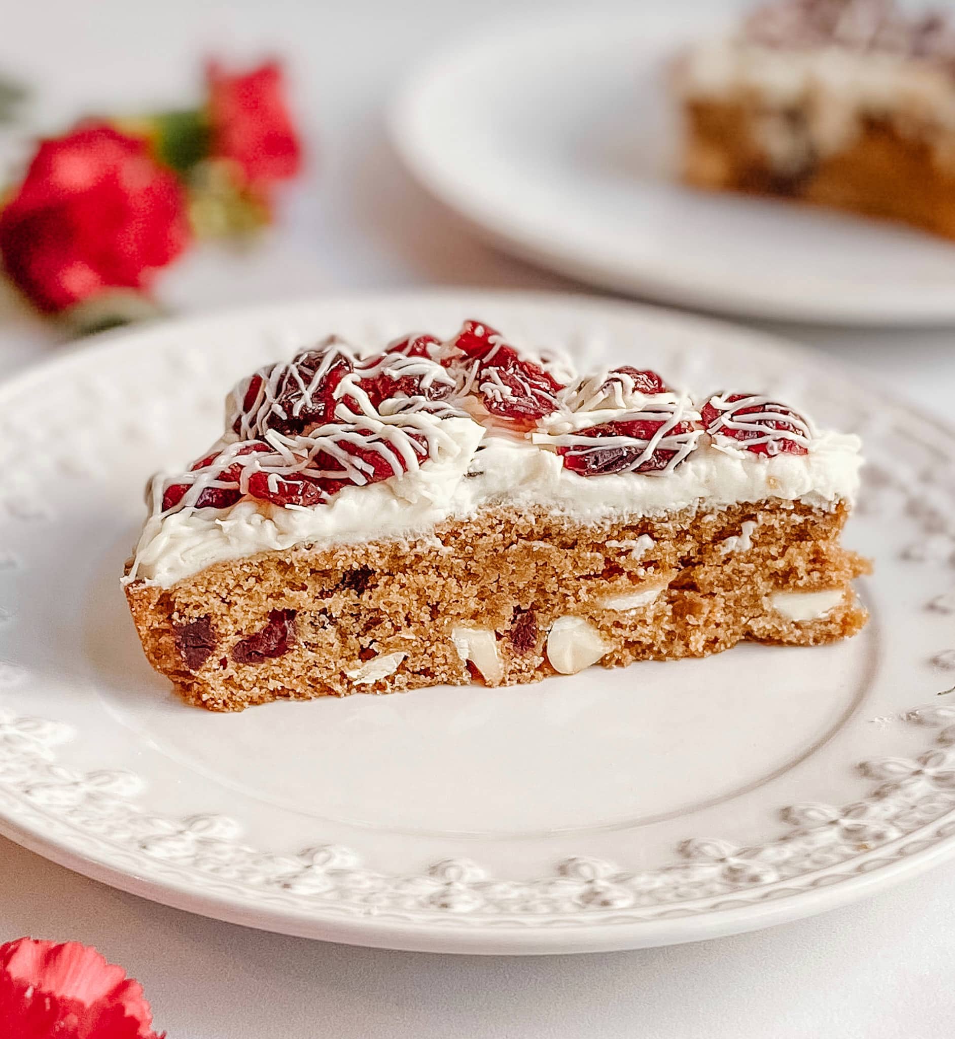 A single gluten-free cranberry bliss bar on plate. Large white chocolate chips and cranberries can be seen in the middle of the bar.