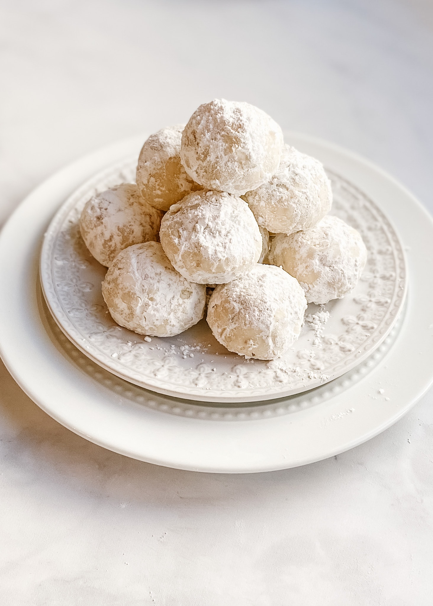 A plate of vegan gluten-free snowball cookies piled tall on a white ceramic plate.
