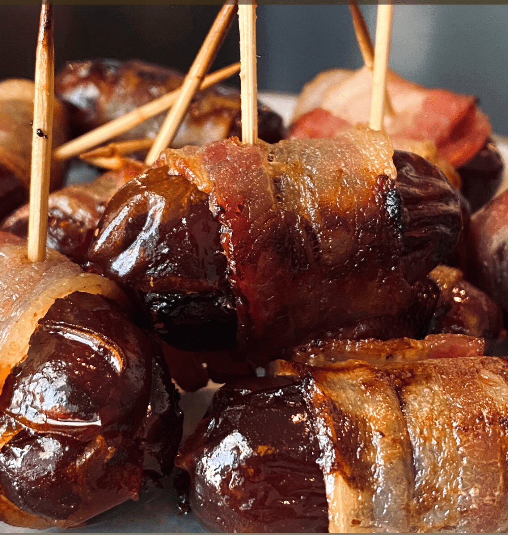 A front view of the bacon wrapped dates. Each date has a toothpick in it and is wrapped in crispy bacon.