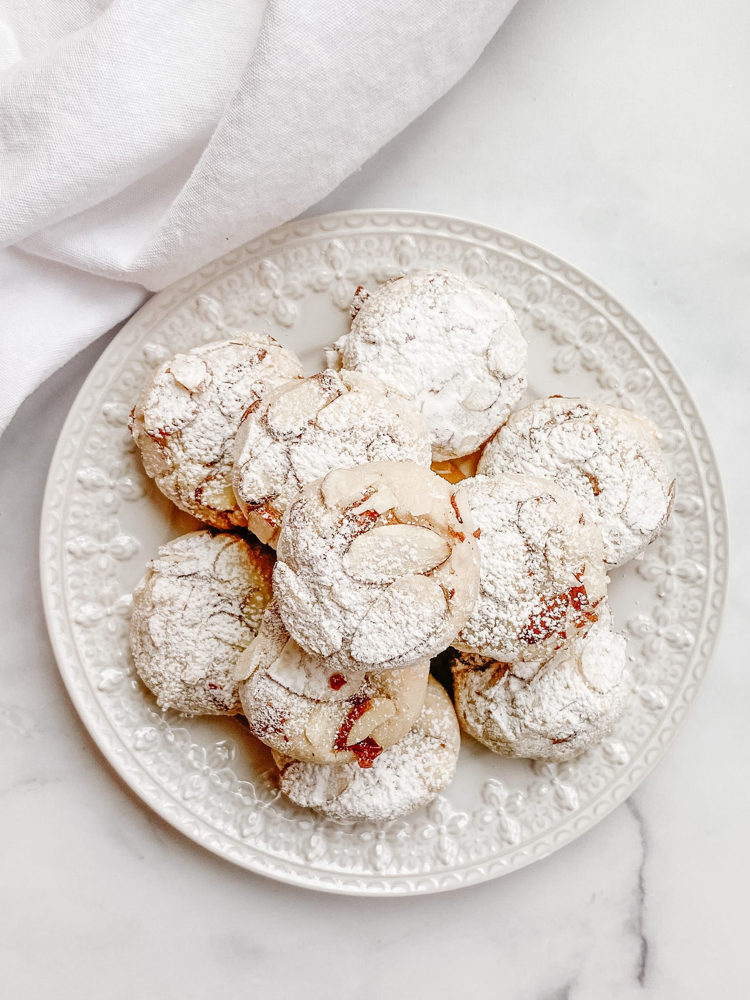 A stack of gluten-free amaretti cookies on a white ceramic plate, being viewed from above.