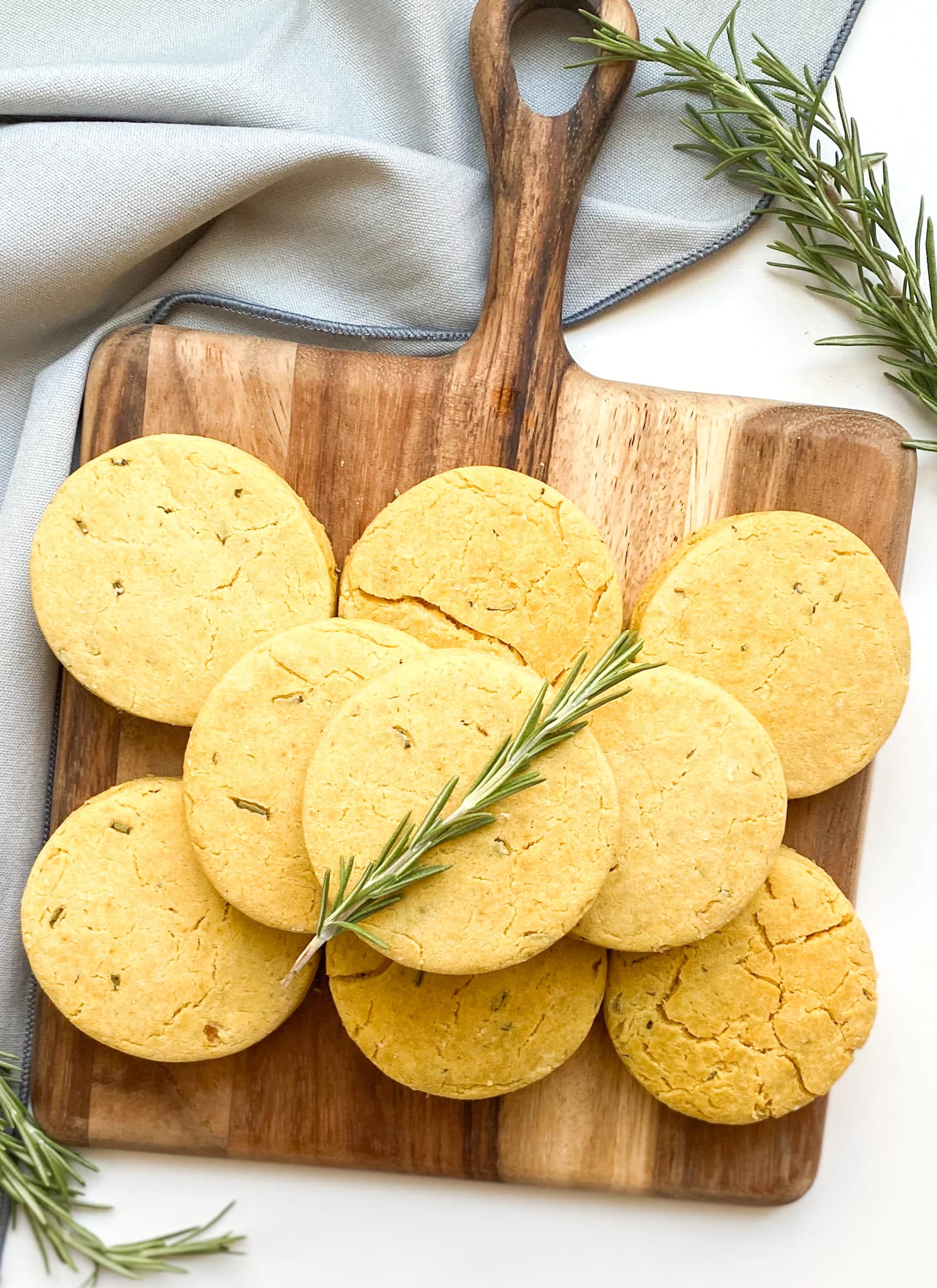 A pile of gluten-free rosemary biscuits on a dark brown cutting board.
