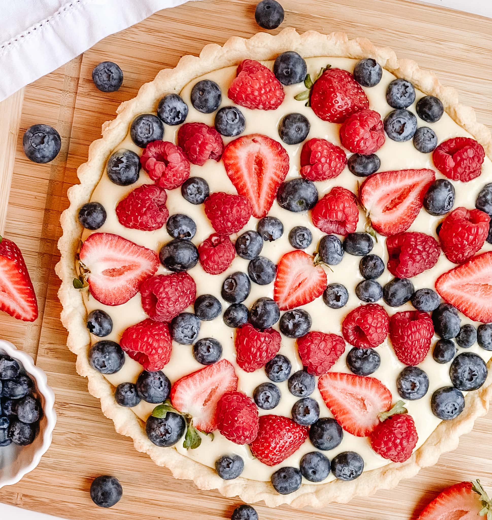 A photo of the vanilla cream fruit tart partially cropped and on a wooden cutting board.