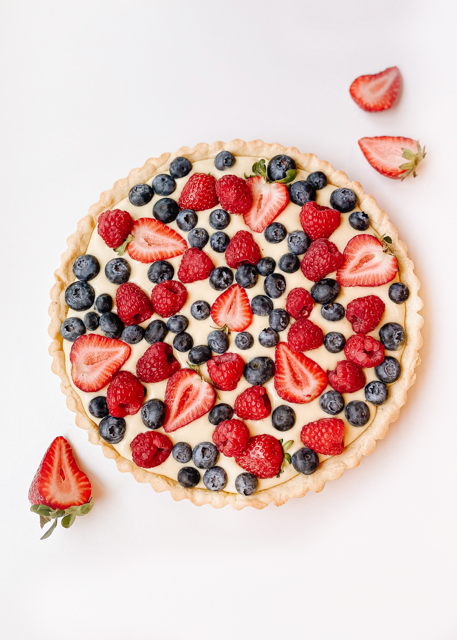 A whole vanilla cream fruit tart photo, shot from above. The top of the fruit tart is topped with blueberries, strawberries, and raspberries.