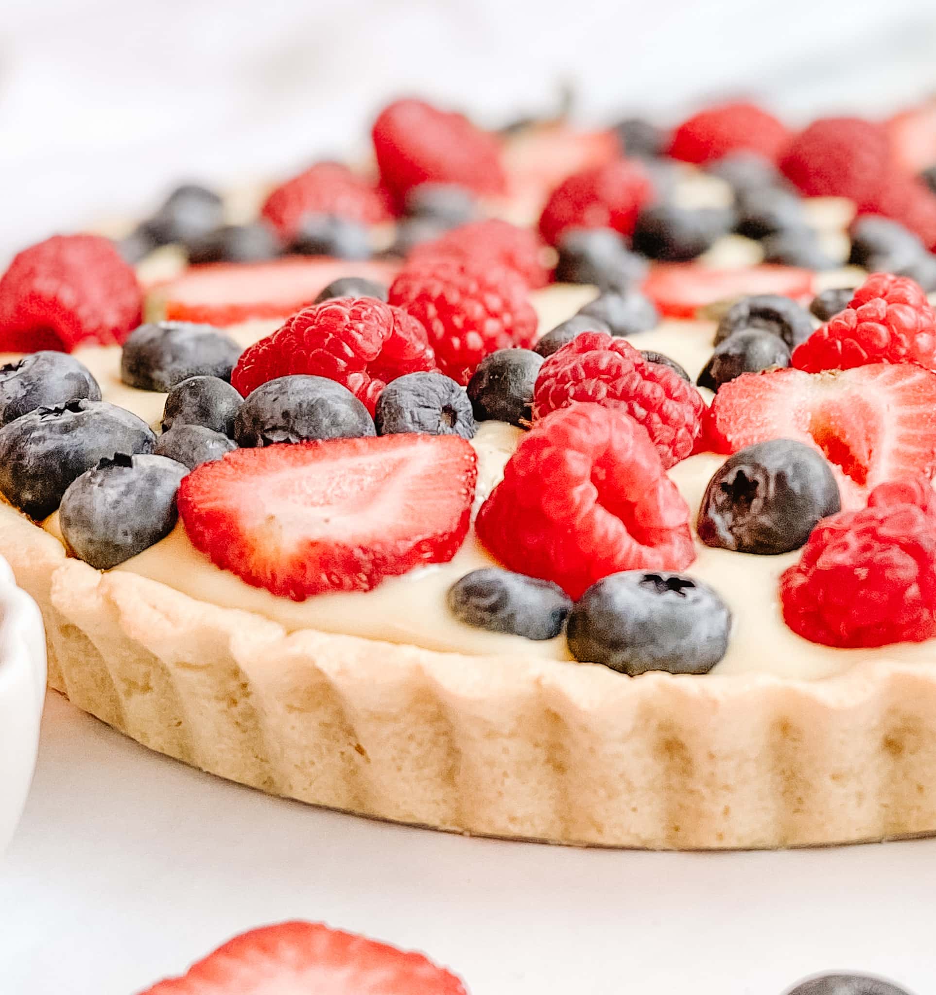 A front shot of the vanilla cream fruit tart. The photo is close up to see the details of the blueberries, strawberries, and raspberries.