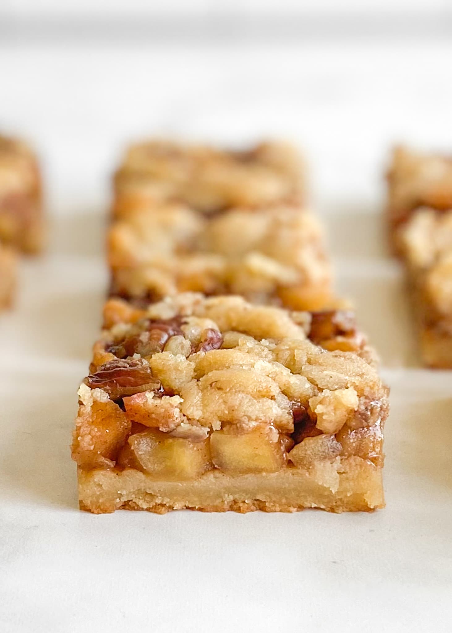 Close up of gluten-free apple crumble bar layers. The background is out of focus to emphasis the front bar.