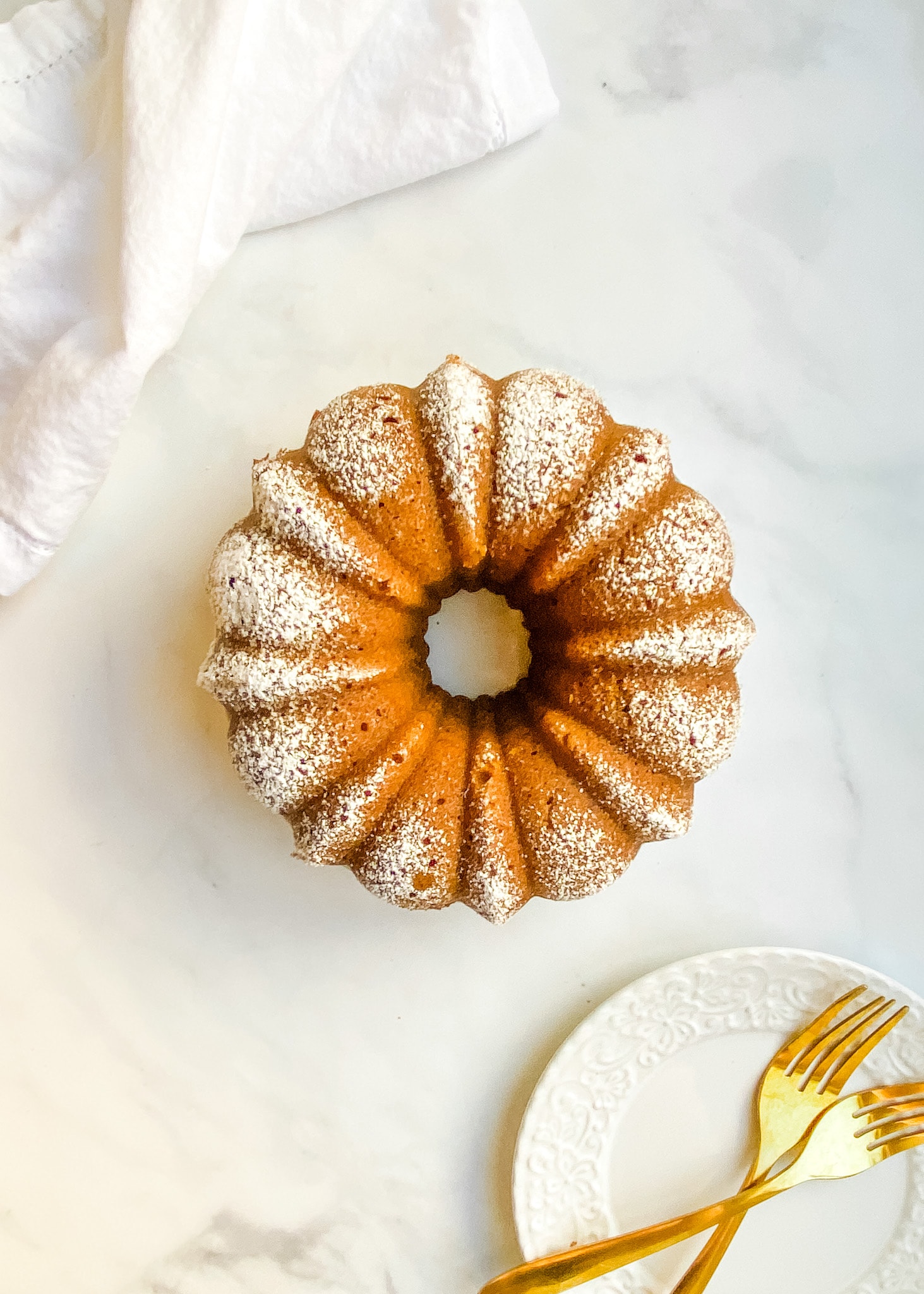 A whole gluten-free pumpkin bundt cake with a dusting of powdered sugar.