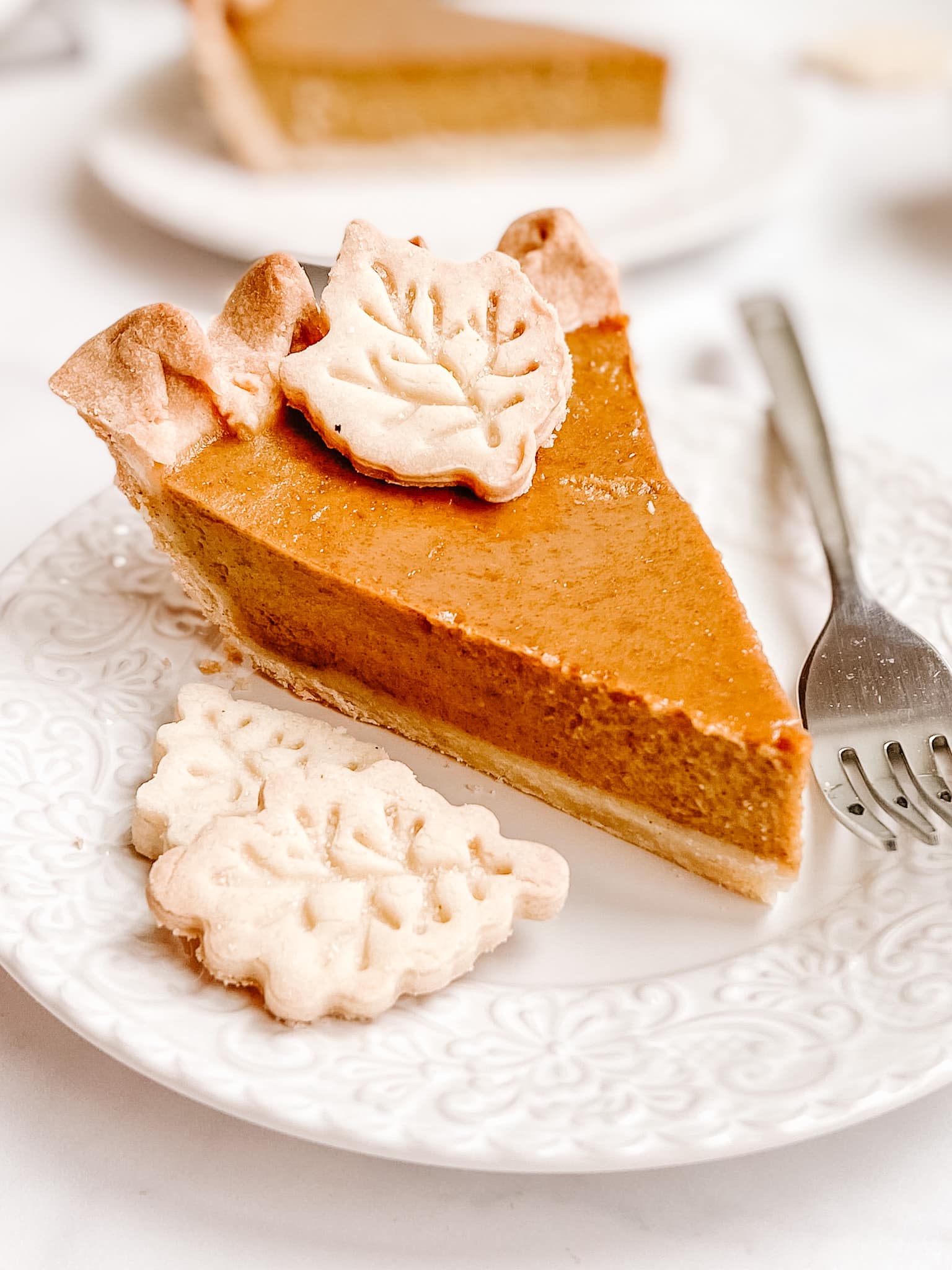 slice of pumpkin pie on lattice decorative white plate with silver fork and pastry leaves 
