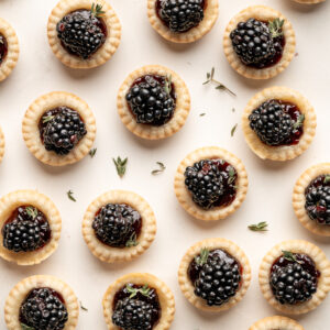 this is a photo of all the blackberry tartlets spread across a light colored backdrop.