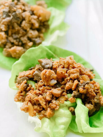 Two gluten-free chicken lettuce wraps. A pile of chicken is in the center of each wrap.