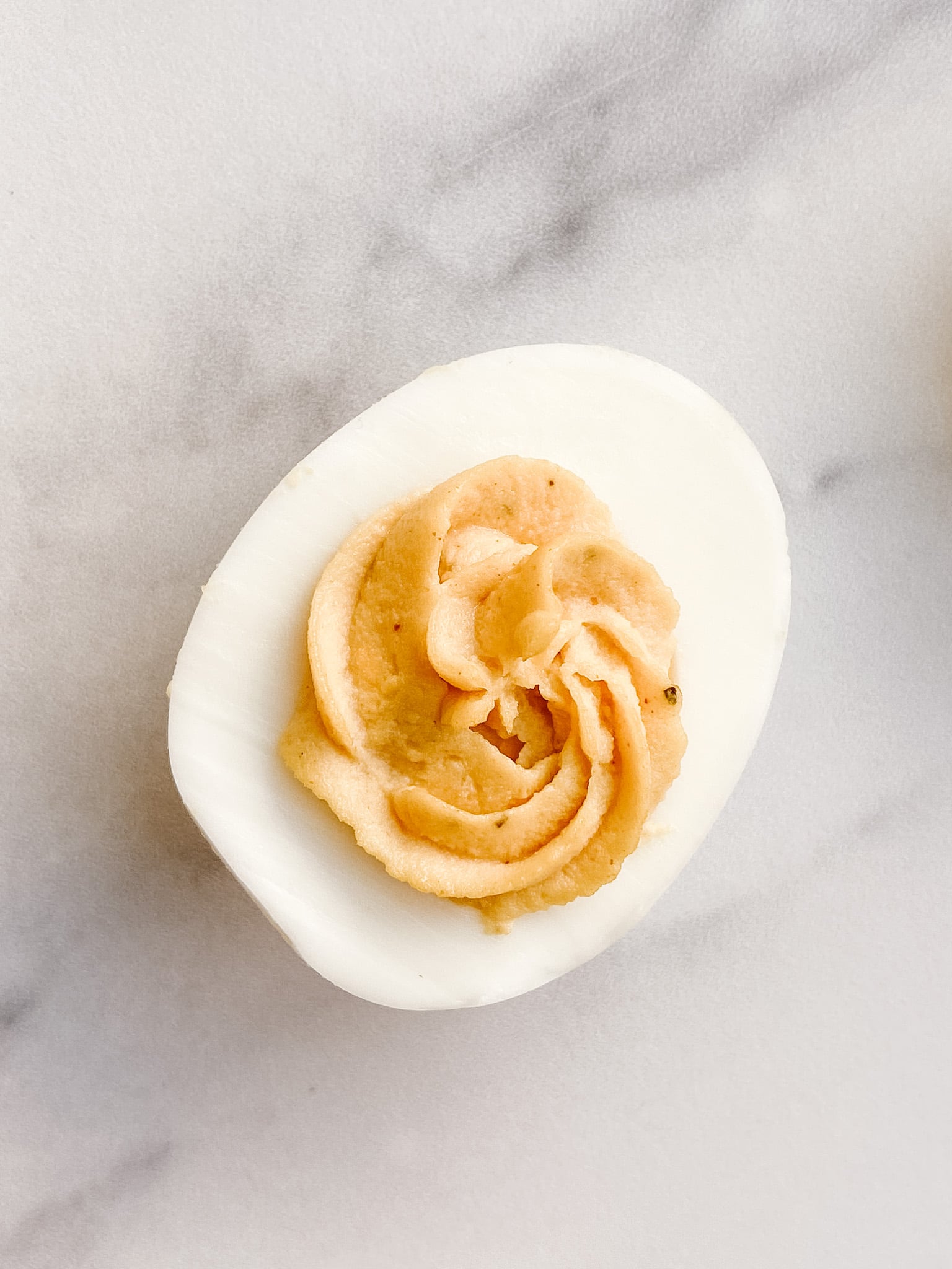 A single classic deviled egg close up. You can see the swirl of the yolk from the piping bag used to fill in the egg.
