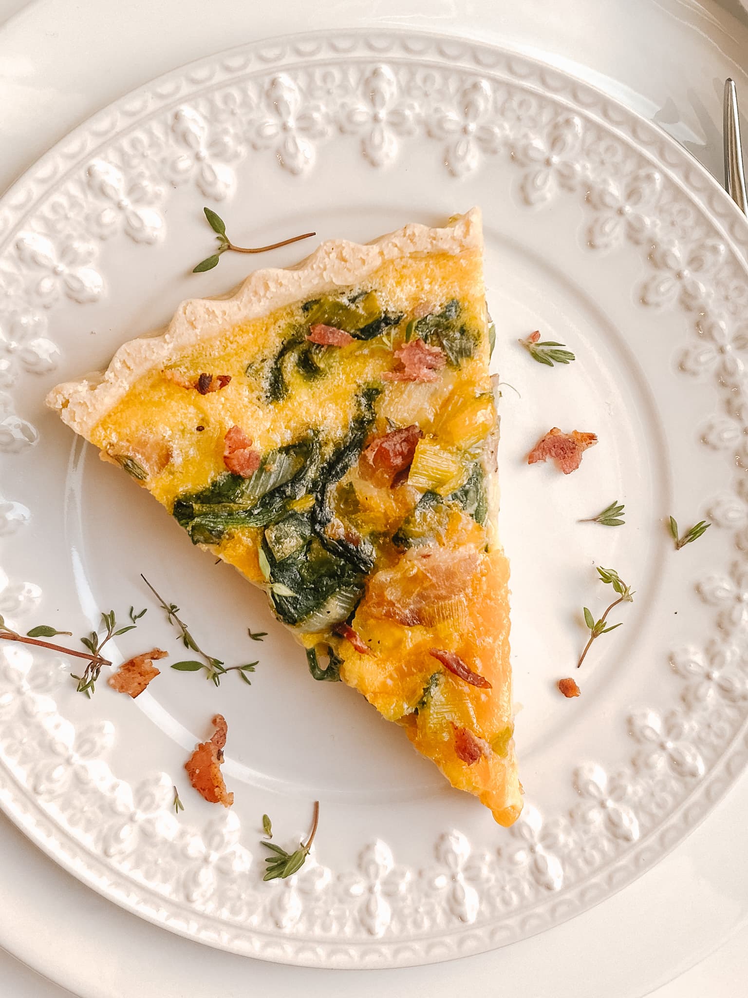zoomed in shot of gluten-free quiche on a white decorative plate, spinach and bacon can be seen clearly