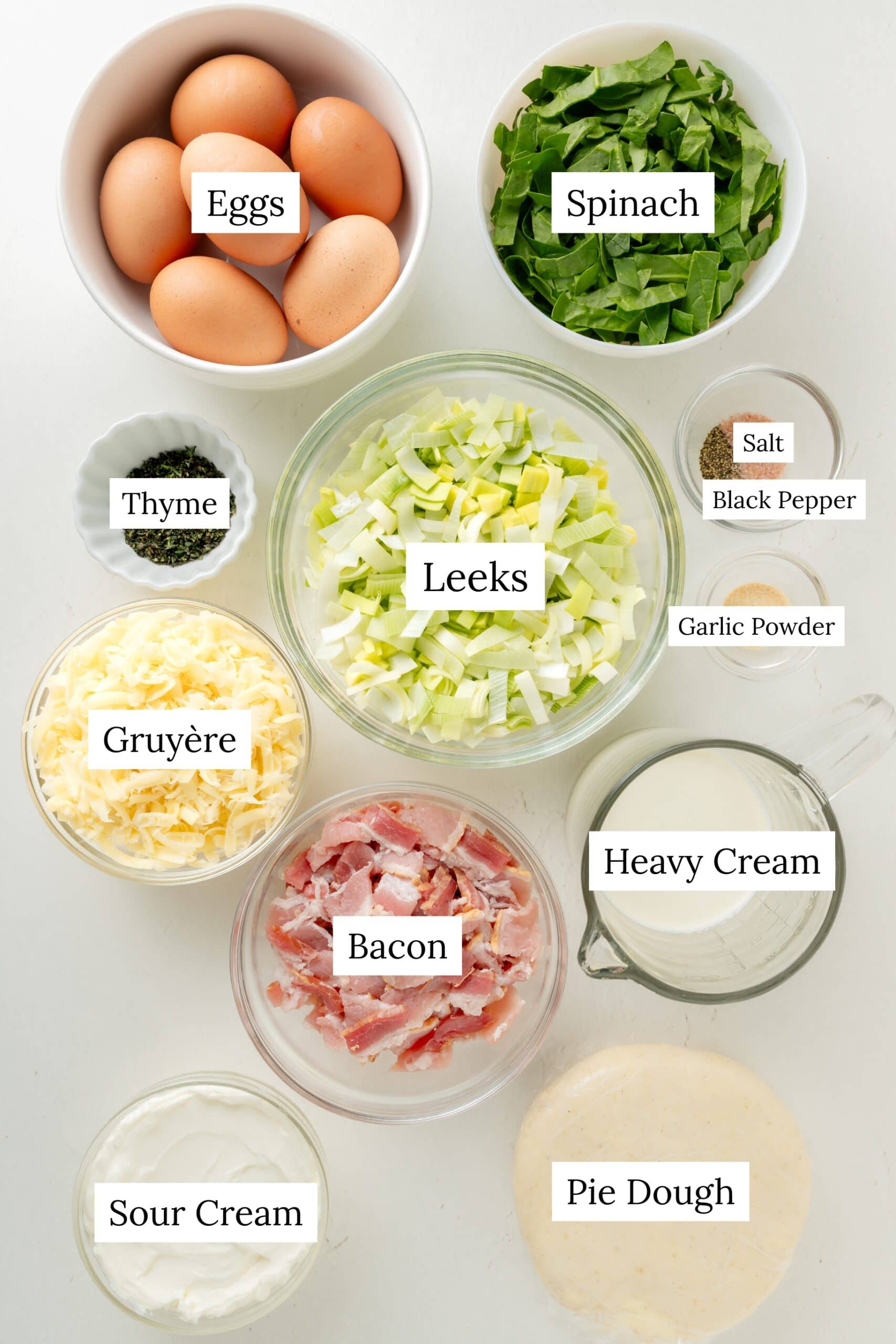 Ingredients for quiche. Eggs, Spinach, salt, black pepper, garlic powder, heavy cream, sour cream, thyme, cheese, bacon, and pie dough.