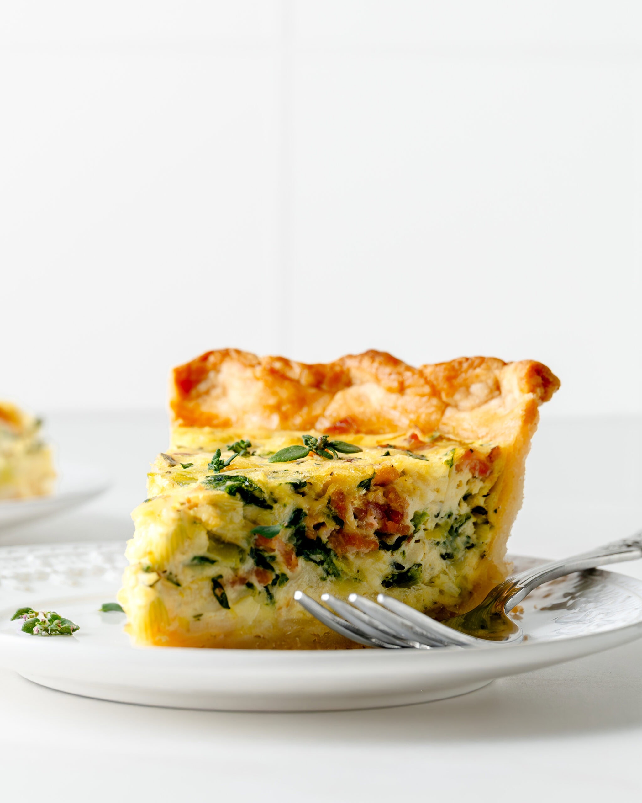 Side view of gluten free quiche with a silver fork and sprinkle of thyme.