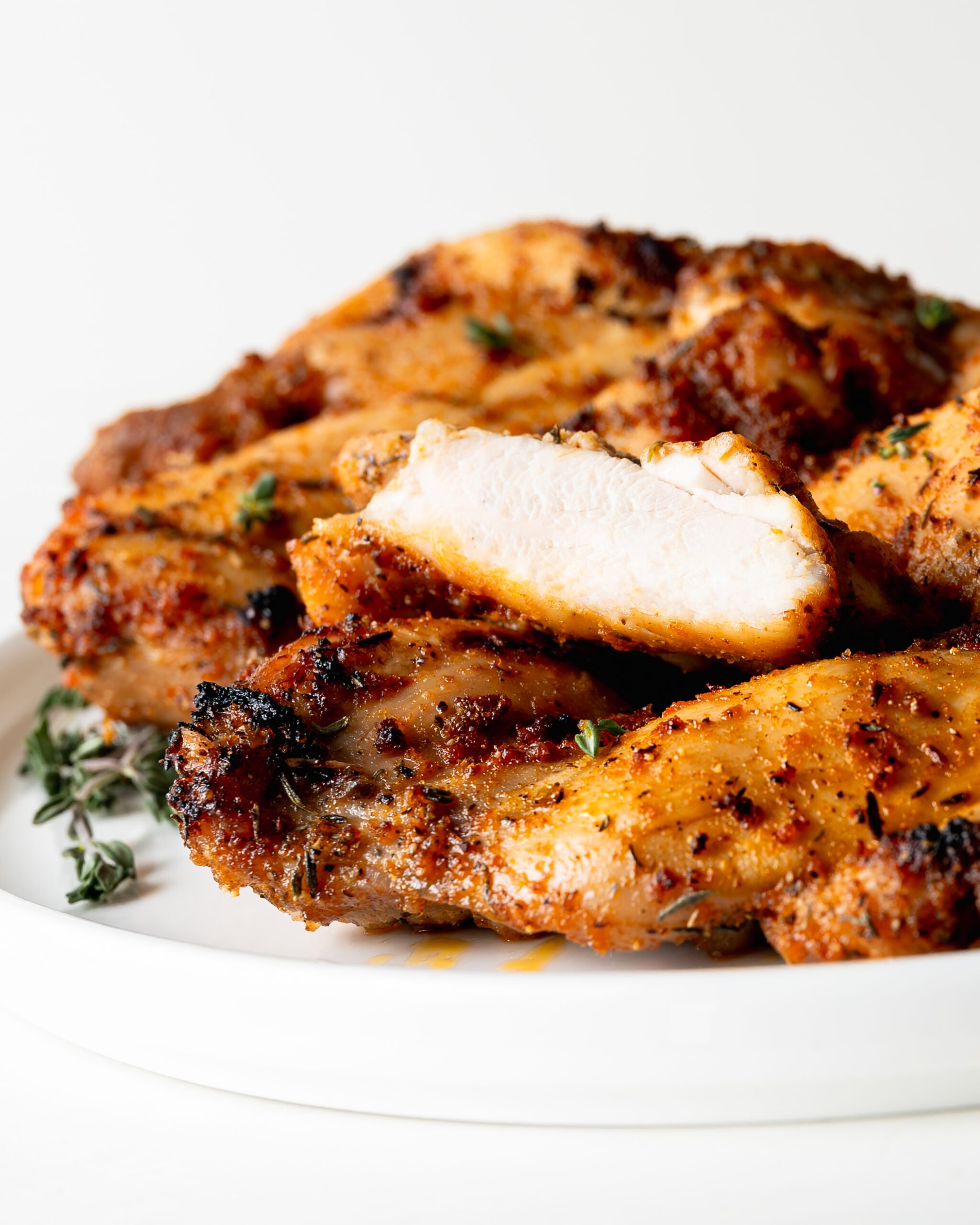 Boneless skinless chicken thighs on a white plate with one of the thighs cut in half, exposing the meat.