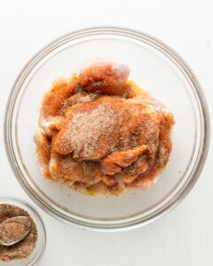 Boneless chicken thighs in a large bowl with oil and spices.
