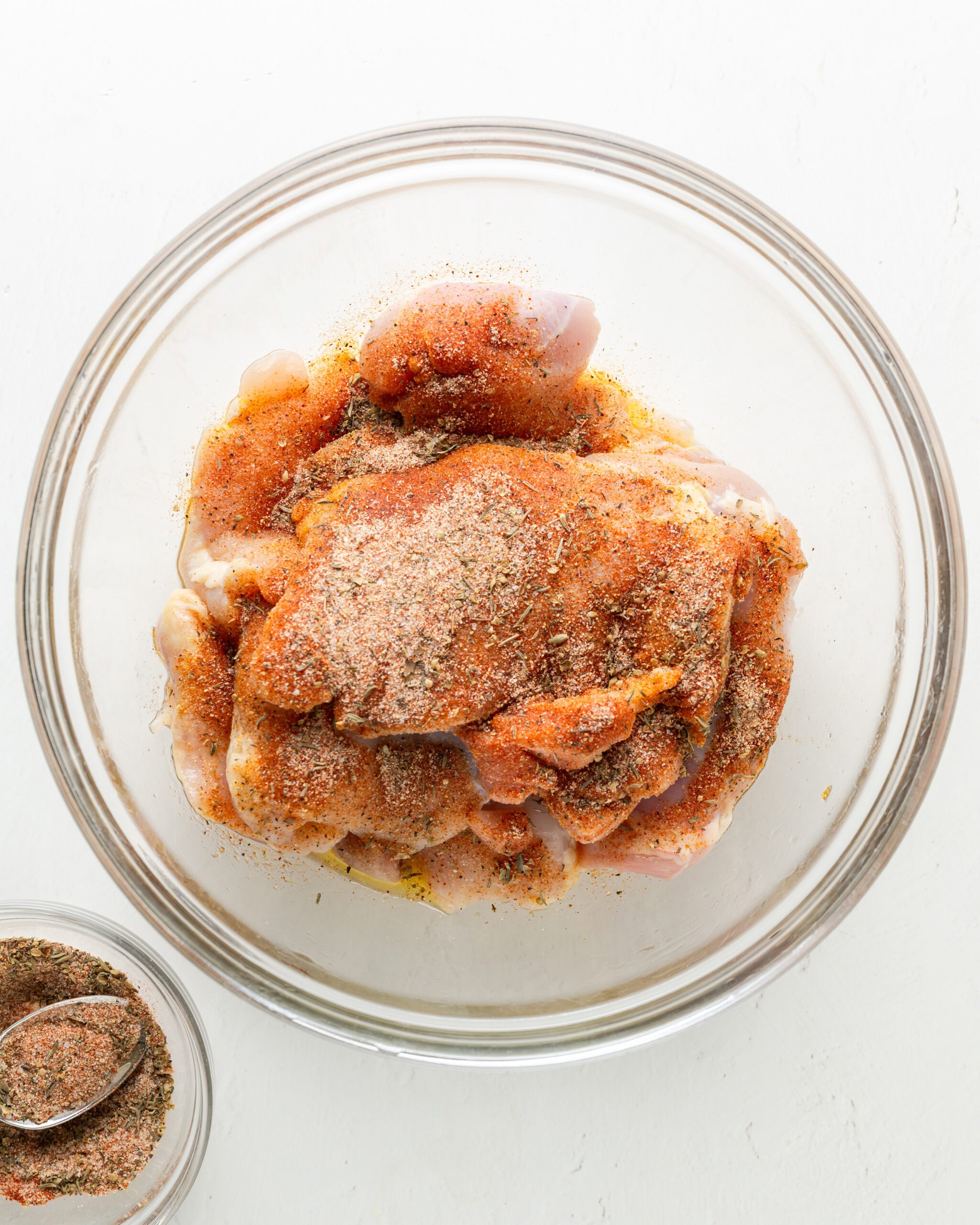 Large clear bowl with chicken and a spice blend sprinkled over the top.