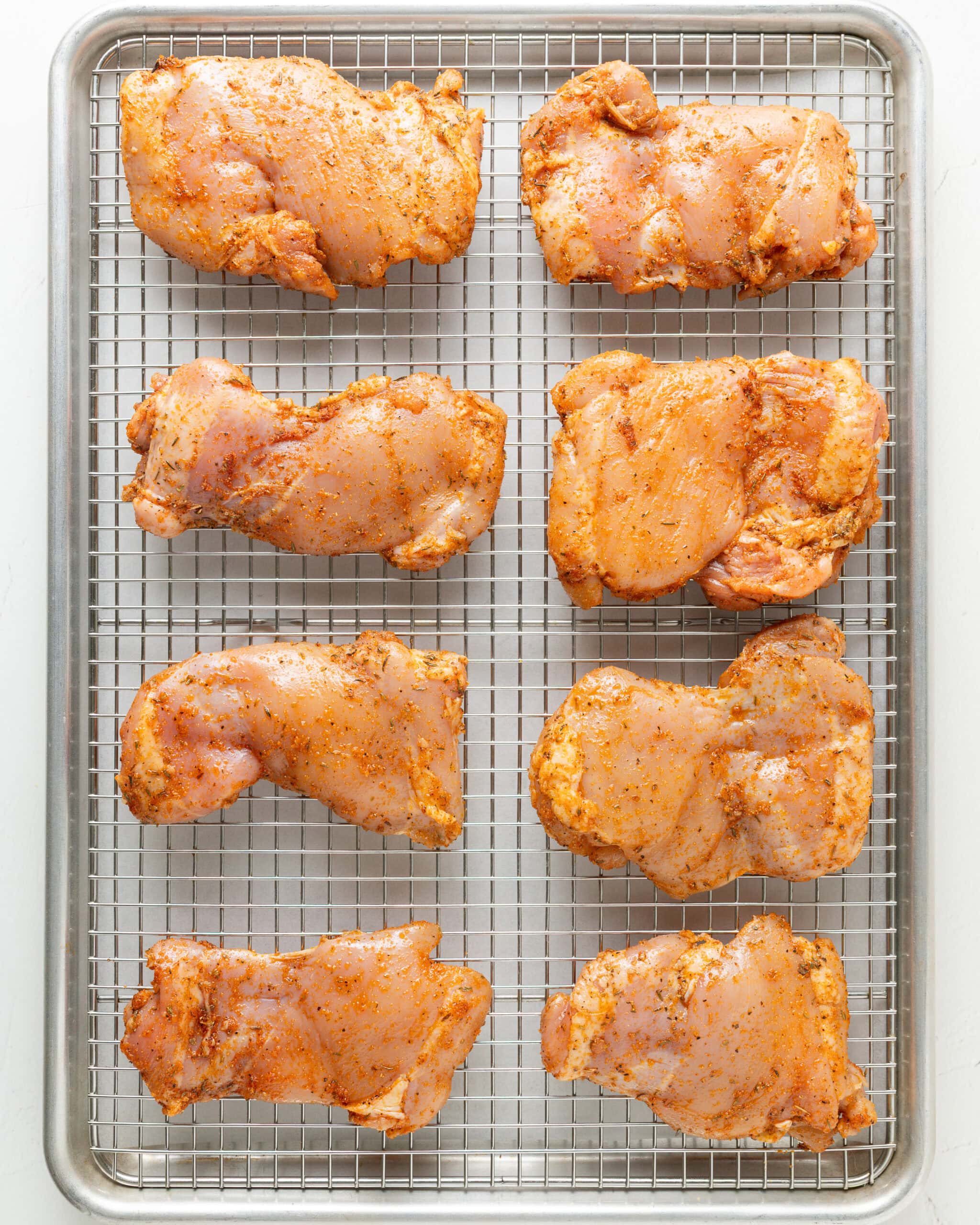 Chicken thighs on top of a baking rack, oiled and spiced.