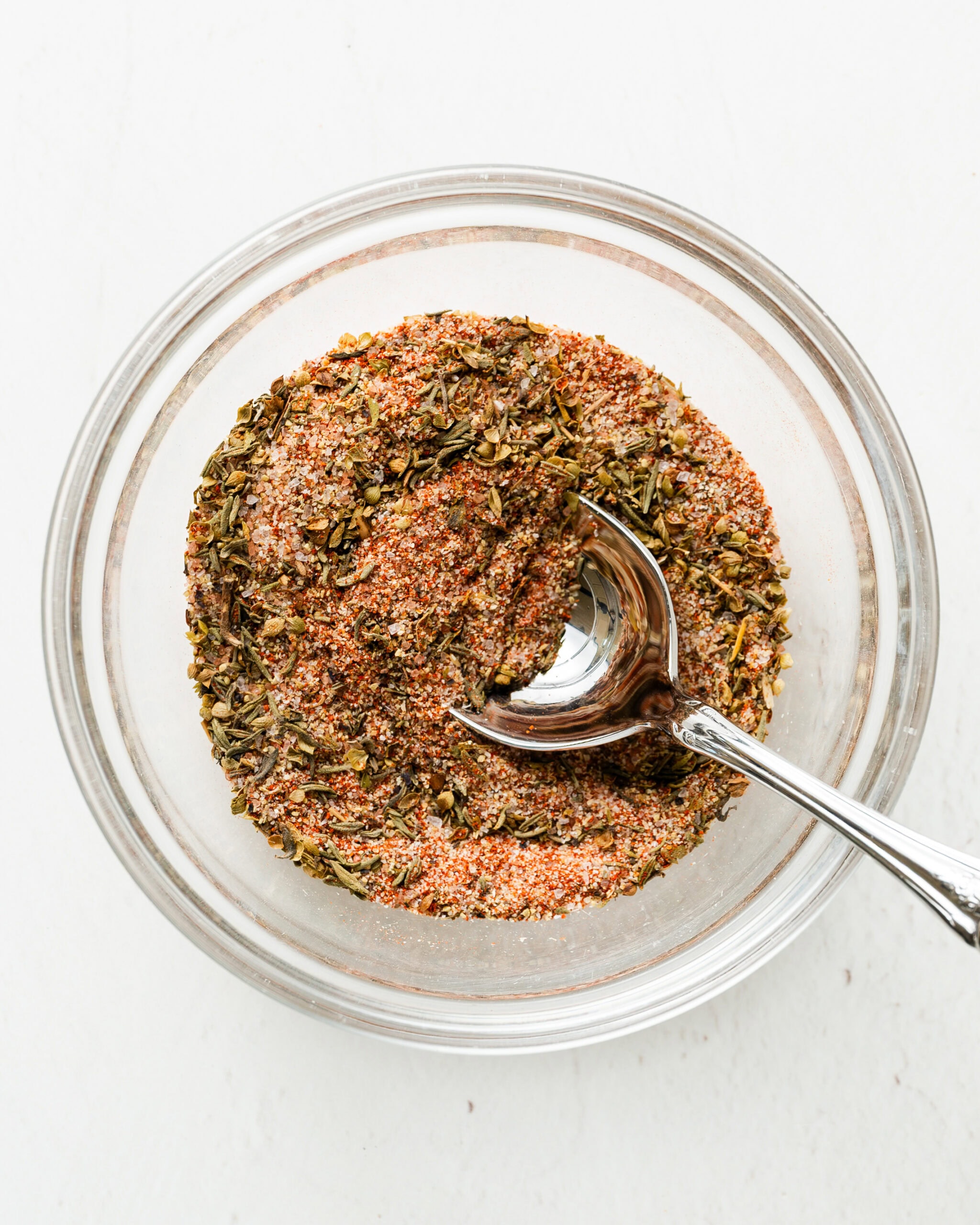 Clear bowl with spices and a silver spoon mixing the spices together.