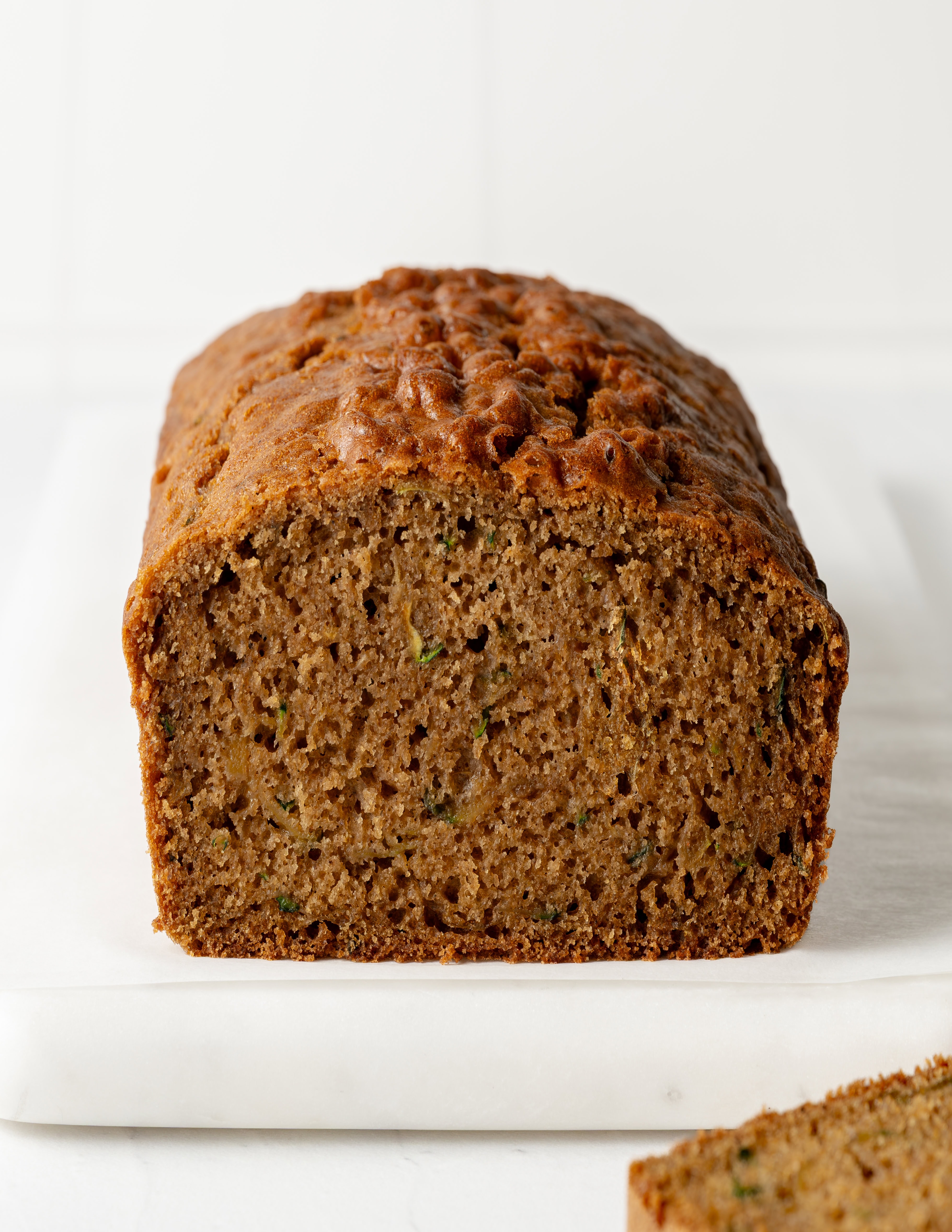Straight-on eye-level view focusing on the interior crumb of a sliced gluten-free zucchini bread loaf resting on parchment paper over a marble surface.