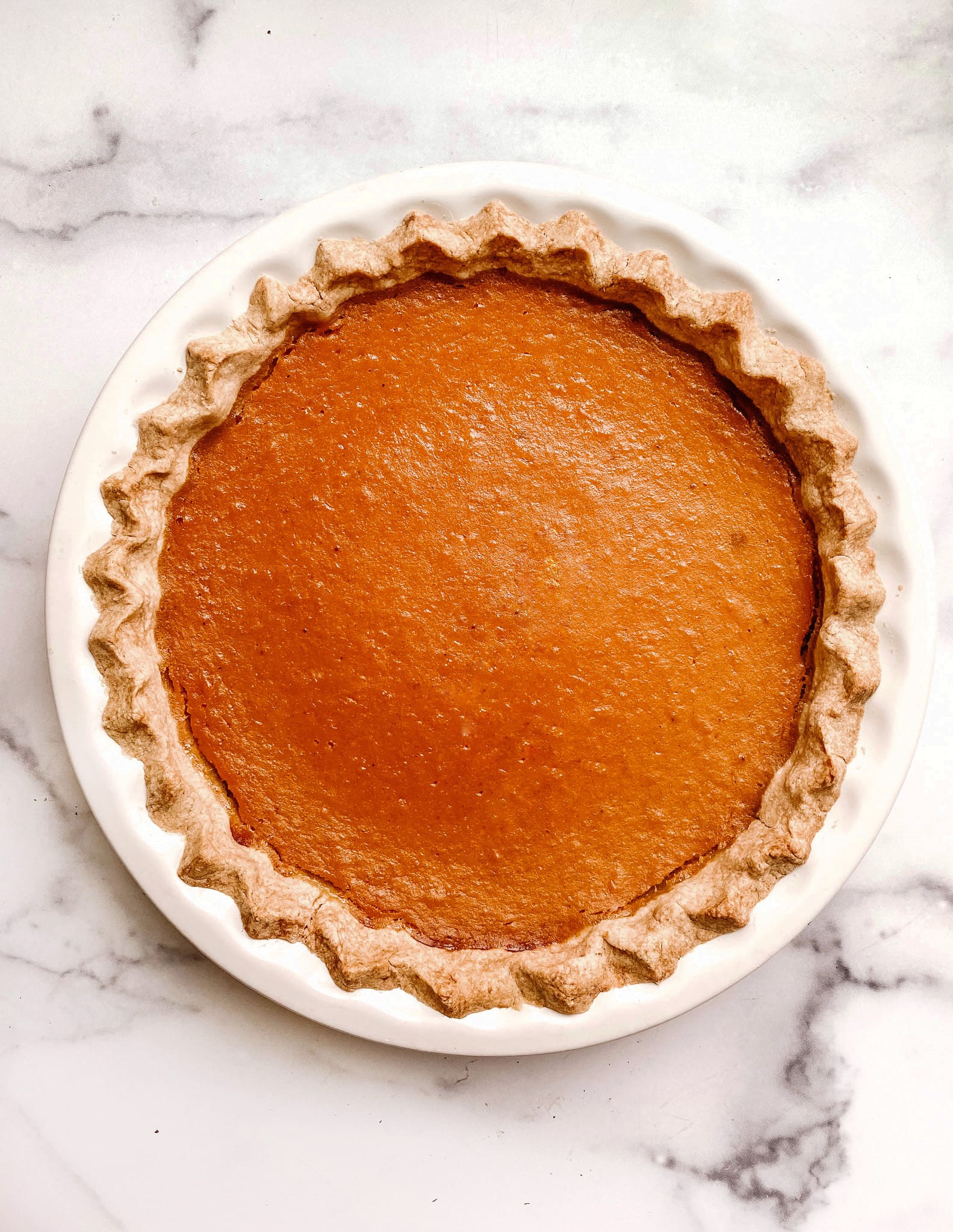 gluten-free sweet potato pie with a smooth orange top in a ceramic white dish on a marble backdrop