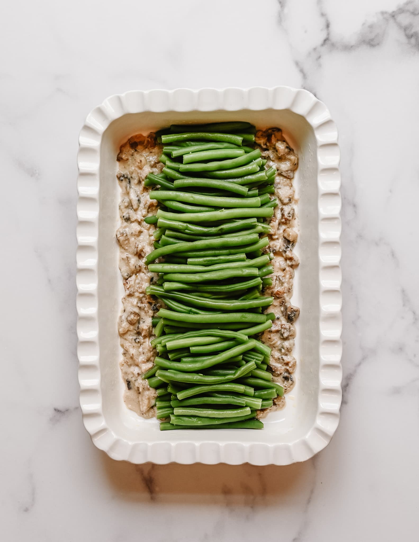 green bean casserole evenly displayed in a white fluted ceramic baking dish.