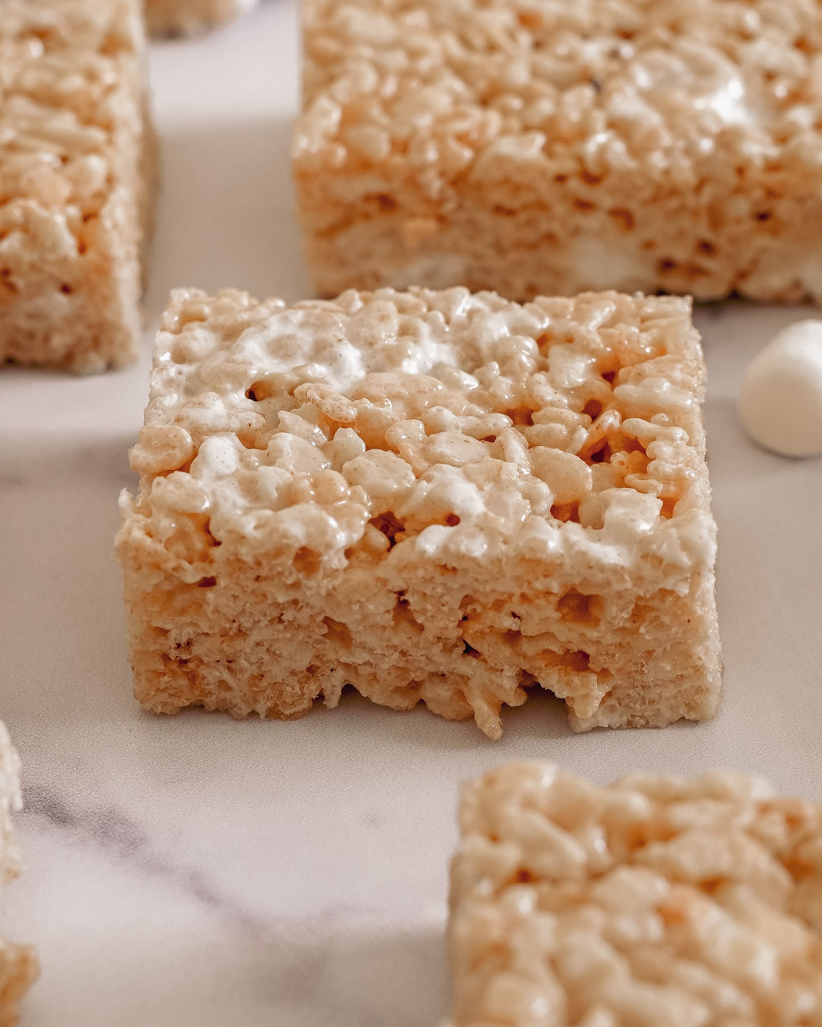 Top view of several rice krispie treats focussed on one center rice krispies treat in the middle on a marble board.