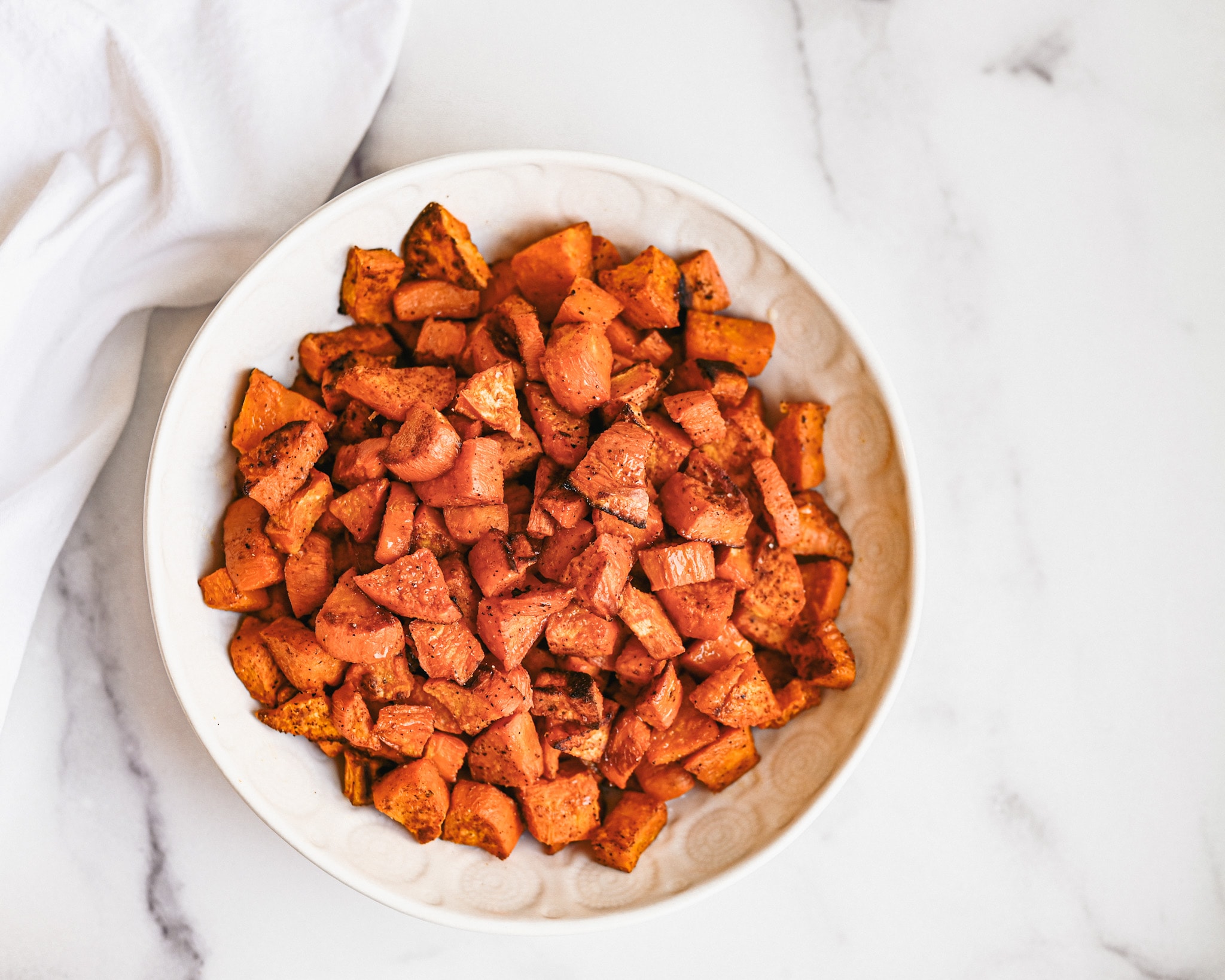 A zoomed out look at roasted sweet potatoes in white bowl on granite top