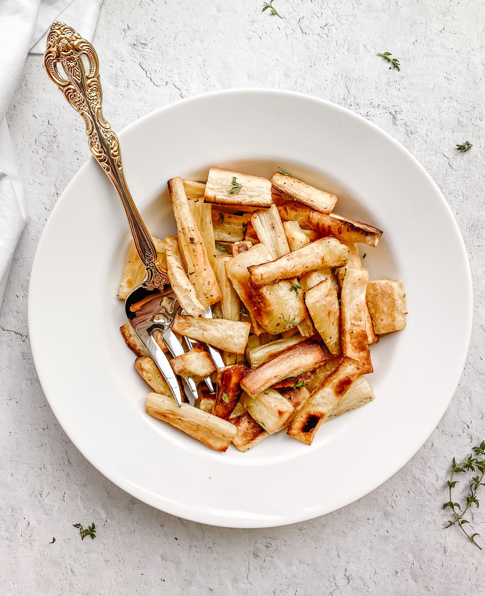 roasted parsnips in a while bowl with a gold serving fork