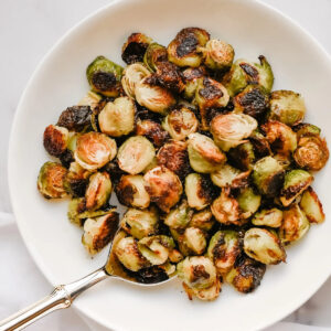A serving bowl filled with crispy oven roasted brussels sprouts.