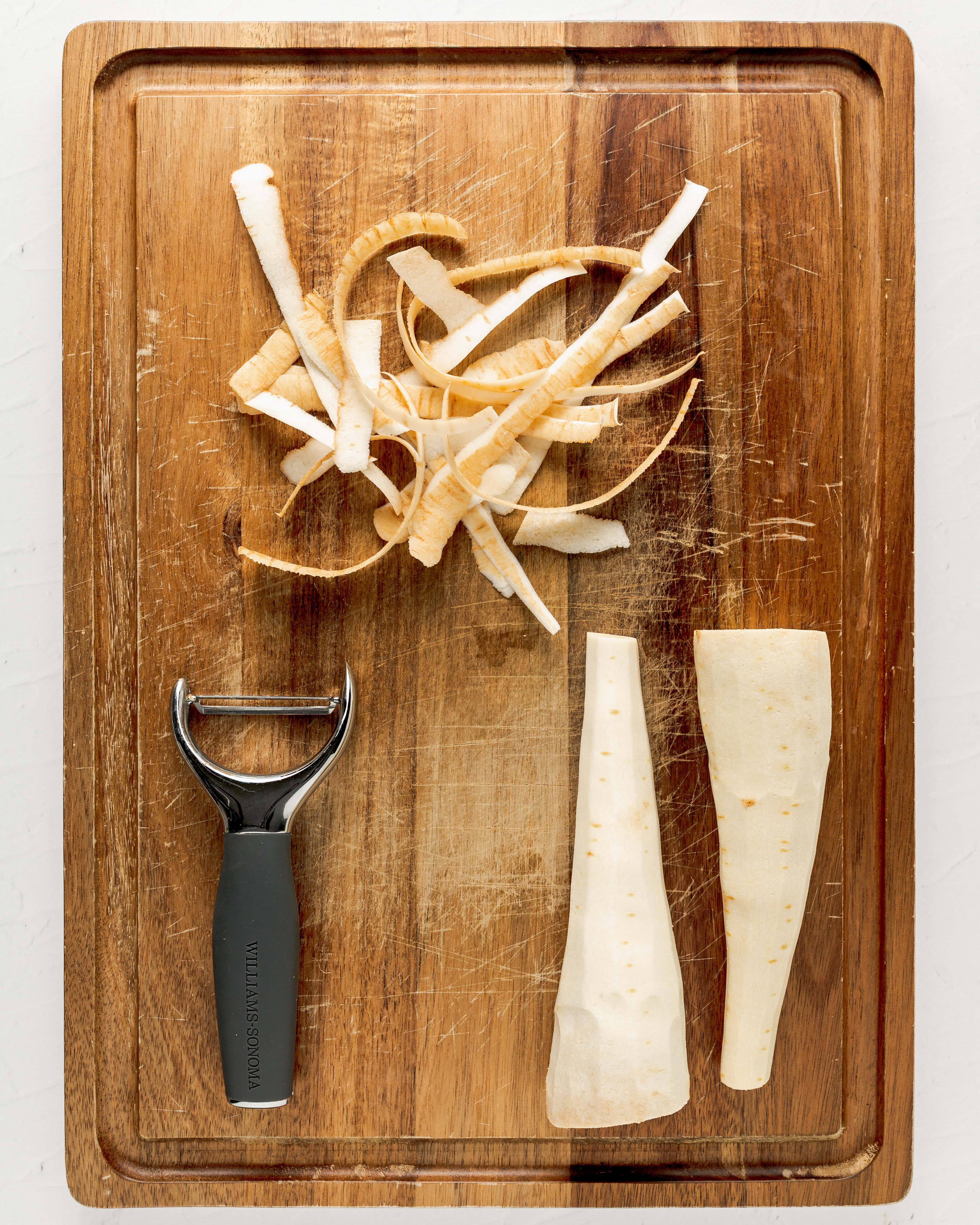 Peeling parsnips with a vegetable peeling on a large wooden cutting board.