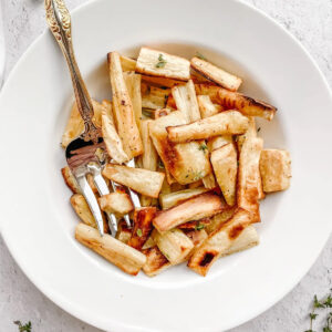 AN image of roasted parsnips in a white serving bowl.