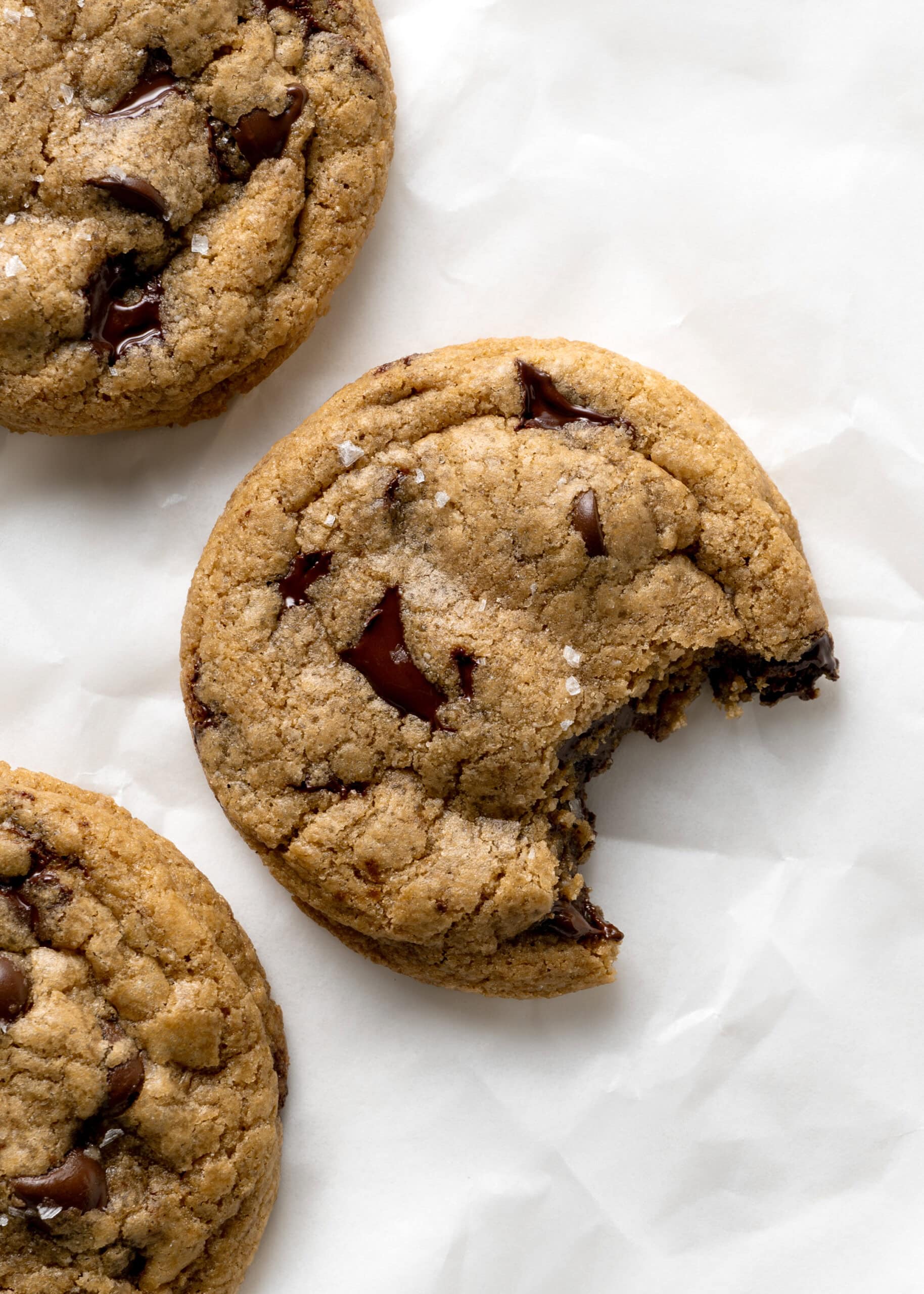 Three coconut oil chocolate chip cookies with a bite taken out of the center cookie.