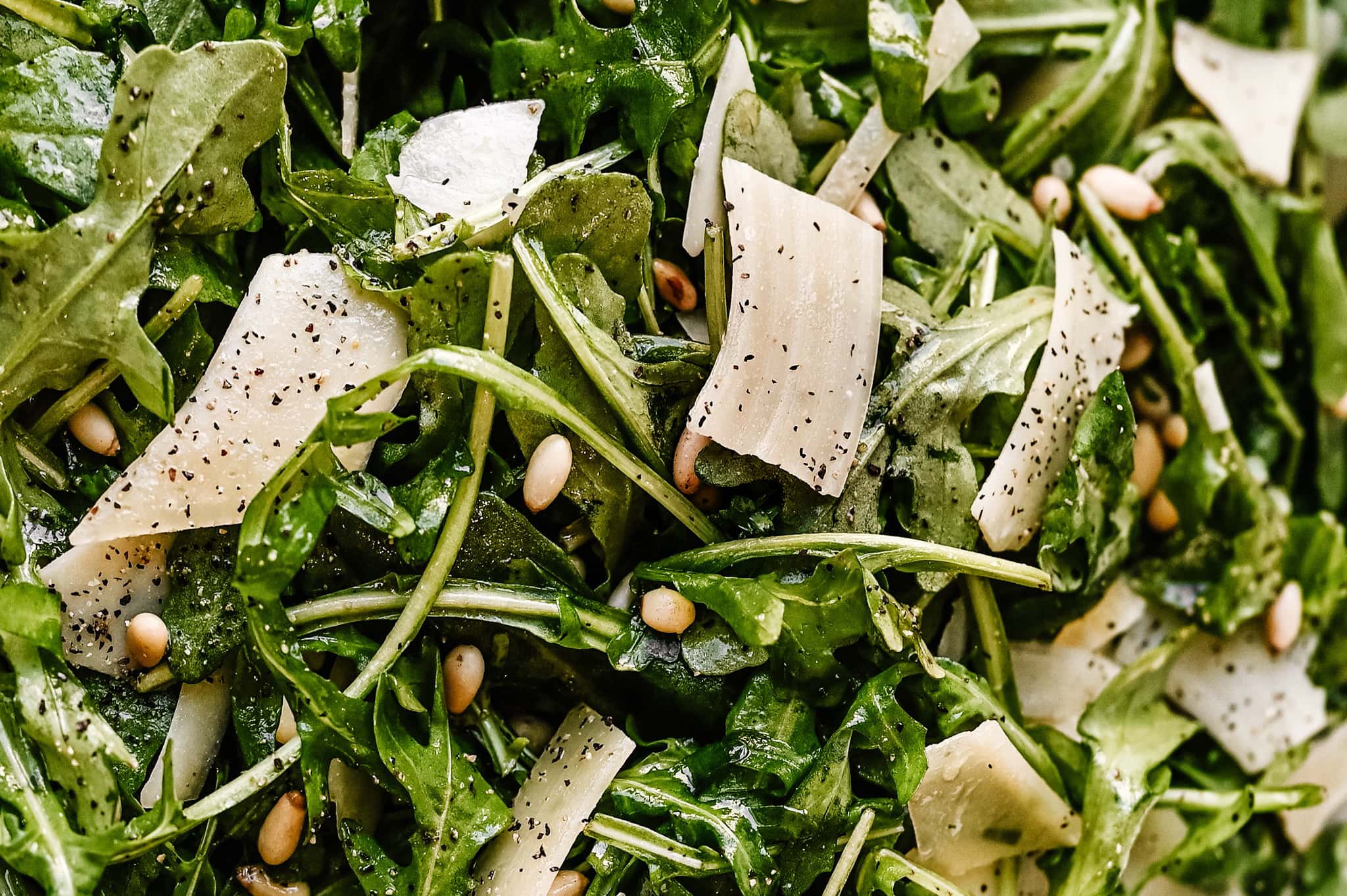close up texture shot of the salad. Pepper, shave parmesan and pine nuts can be seen throughout the salad