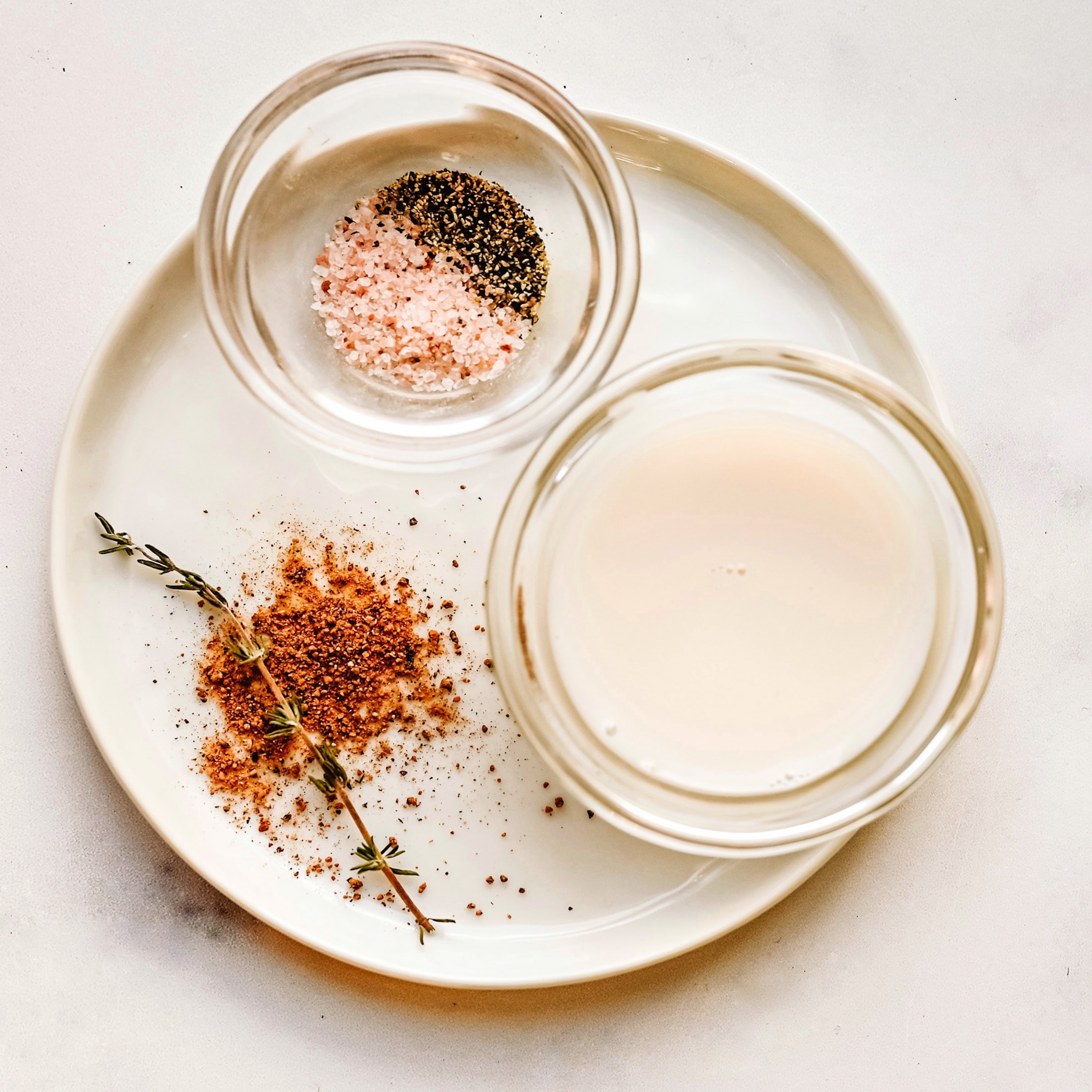 An ingredient seasoning shot, with a small bowl of salt and pepper, coconut milk, and fresh herbs.