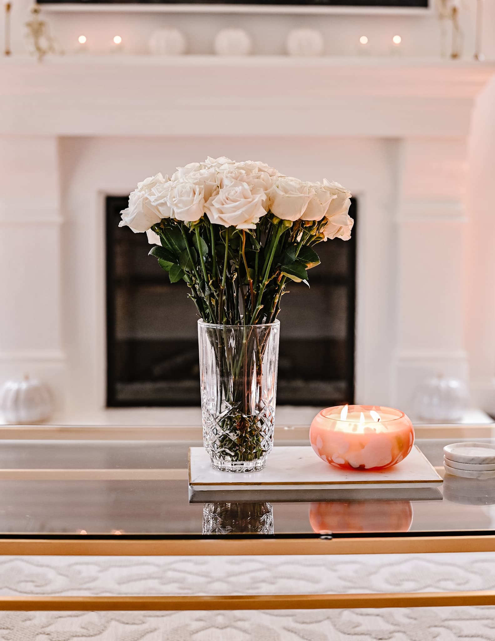 white flowers in a vase on a glass table, a pumpkin scented candle sits next to it. Halloween Home tour living room