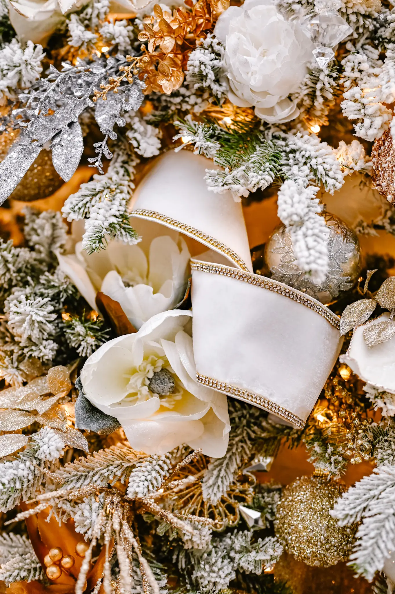 Close up of white and gold ribbons, white flowers and flocked Christmas tree branches.
