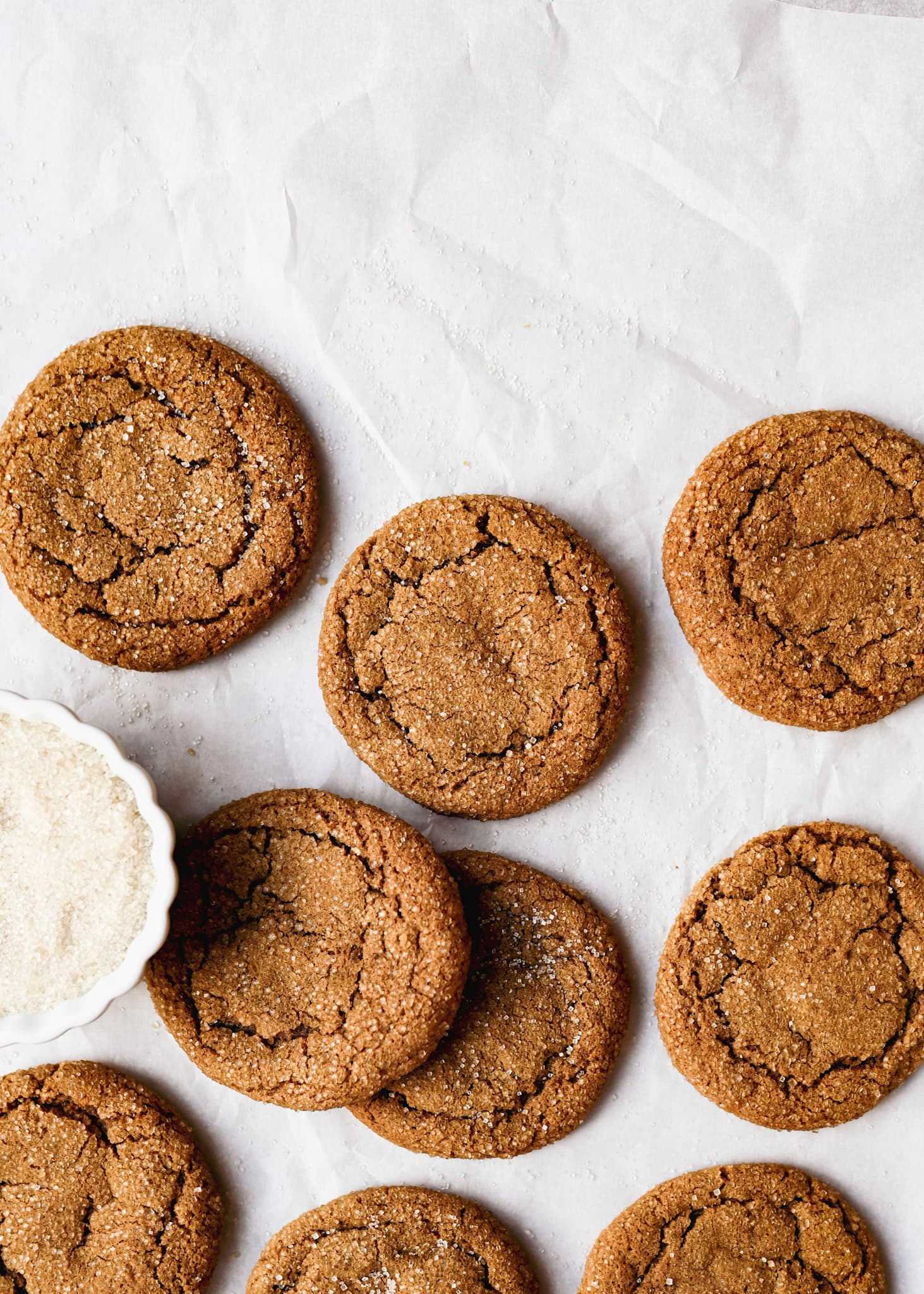 various soft molasses cookies on a white background, with a bowl of sugar 
