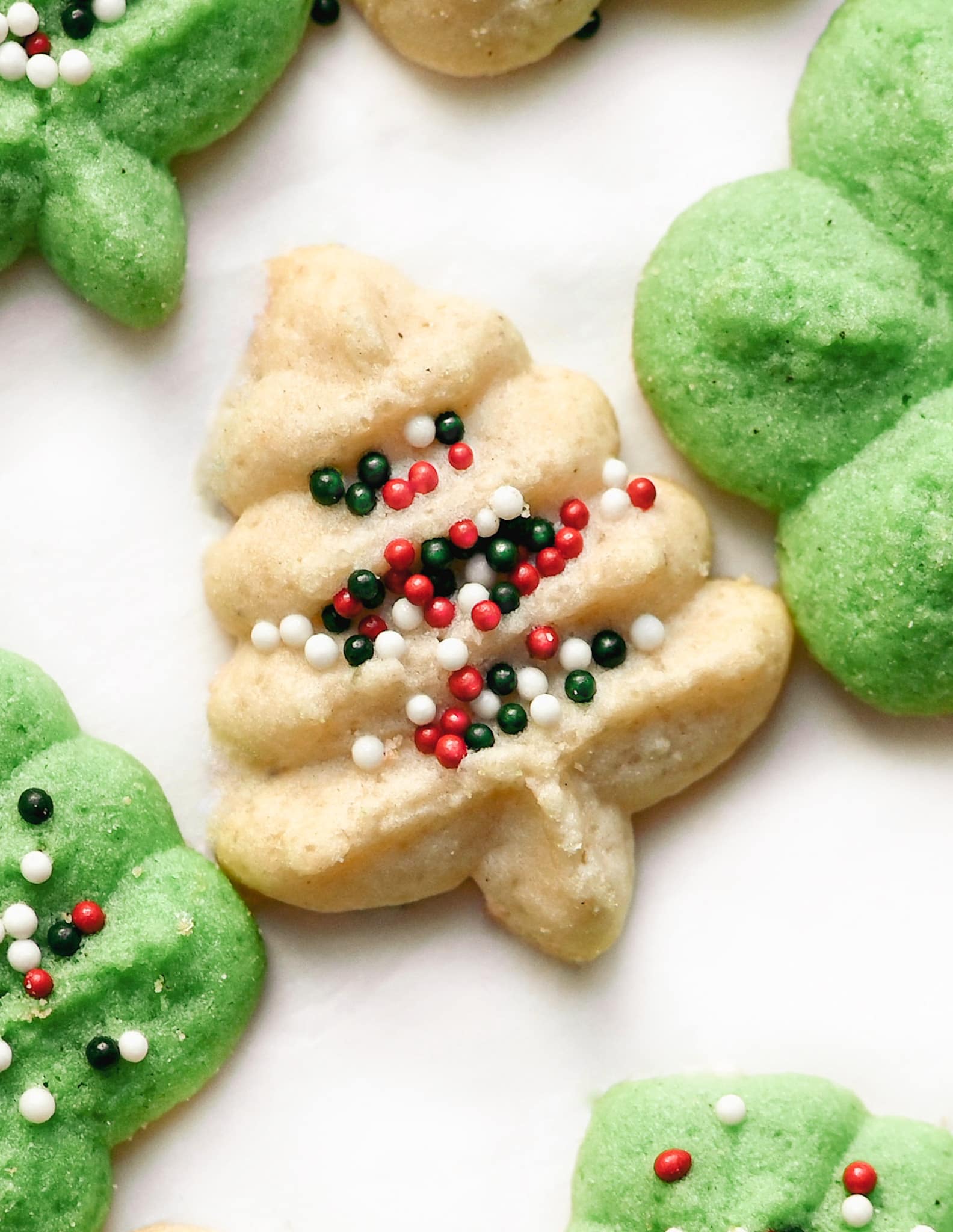 white gluten free spritz cookie with sprinkles. Surrounded by green spritz cookies.