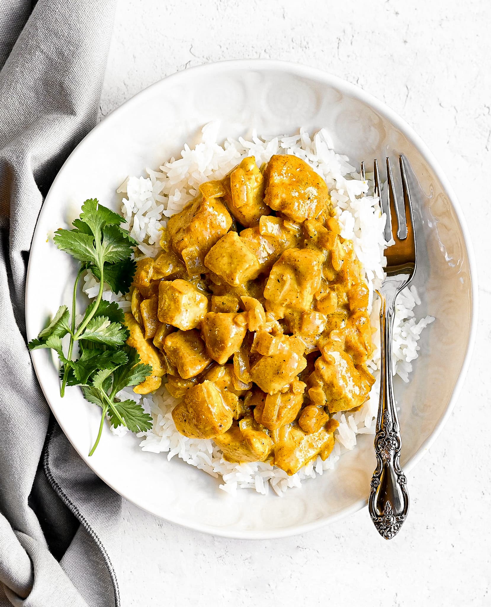 bowl of yellow chicken curry with a grey napkin and silver fork being used for decoration