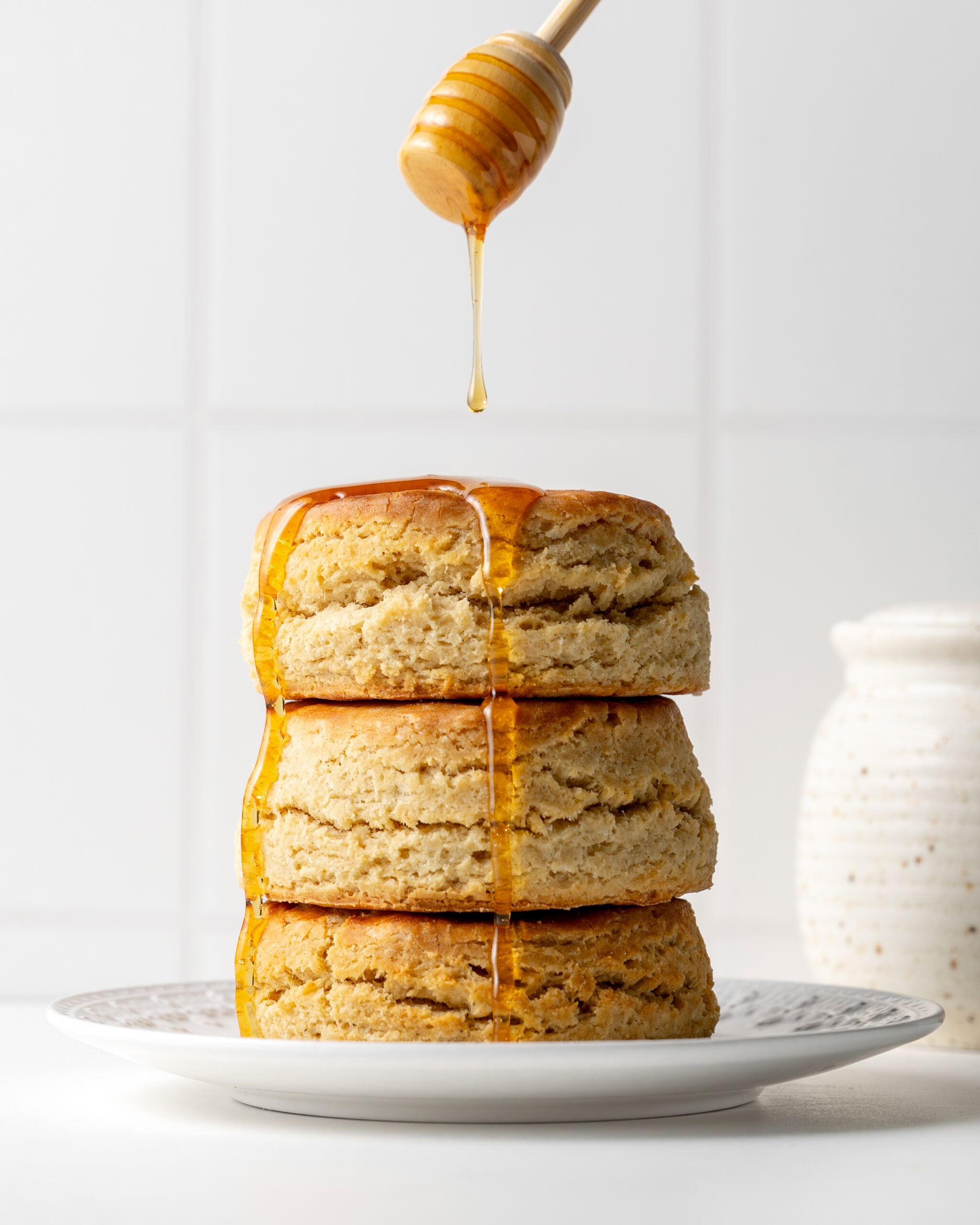Buttermilk biscuits with honey drizzled on top, sitting stacked on a white plate.