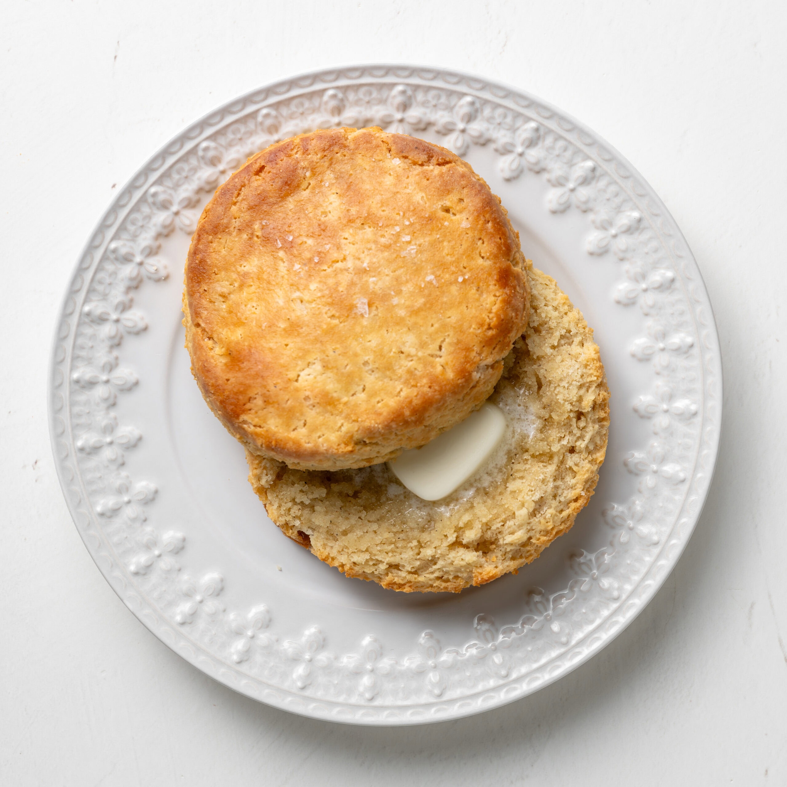 Buttermilk biscuits on a white plate, cut in half with melted butter.