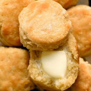 a gluten-free biscuit is cut open on a stack of biscuits, melting butter is on the biscuit.