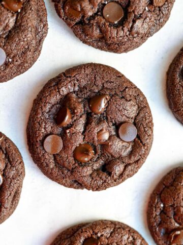 A spread of gluten-free double chocolate chip cookies. A bunch of dark chocolate chips can be seen throughout the cookie.