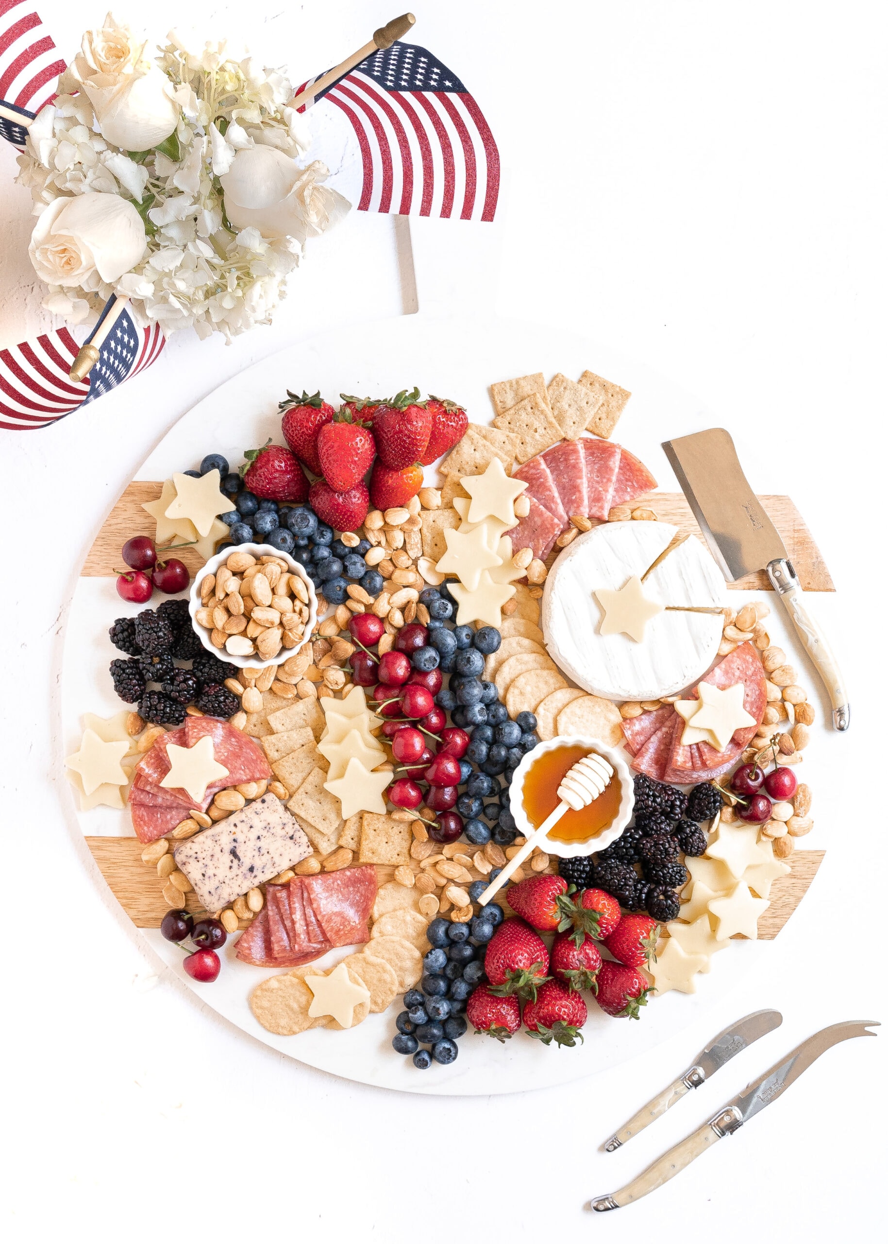 A photo of my patriotic charcuterie board. Made with gluten-free crackers, red and blue fruits, star shaped white cheddar cheese, nuts, and honey.
