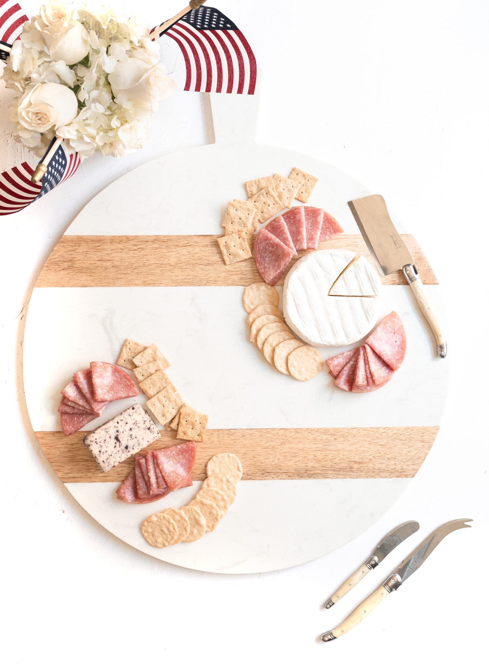 The first photo on how to build your patriotic charcuterie board. First step is to evenly space hard and soft cheeses on the opposite side of the board.