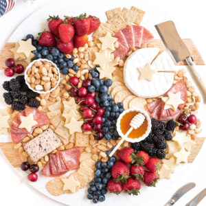 A patriotic charcuterie board photo. Various crackers, cheeses, and fruits make up the board.