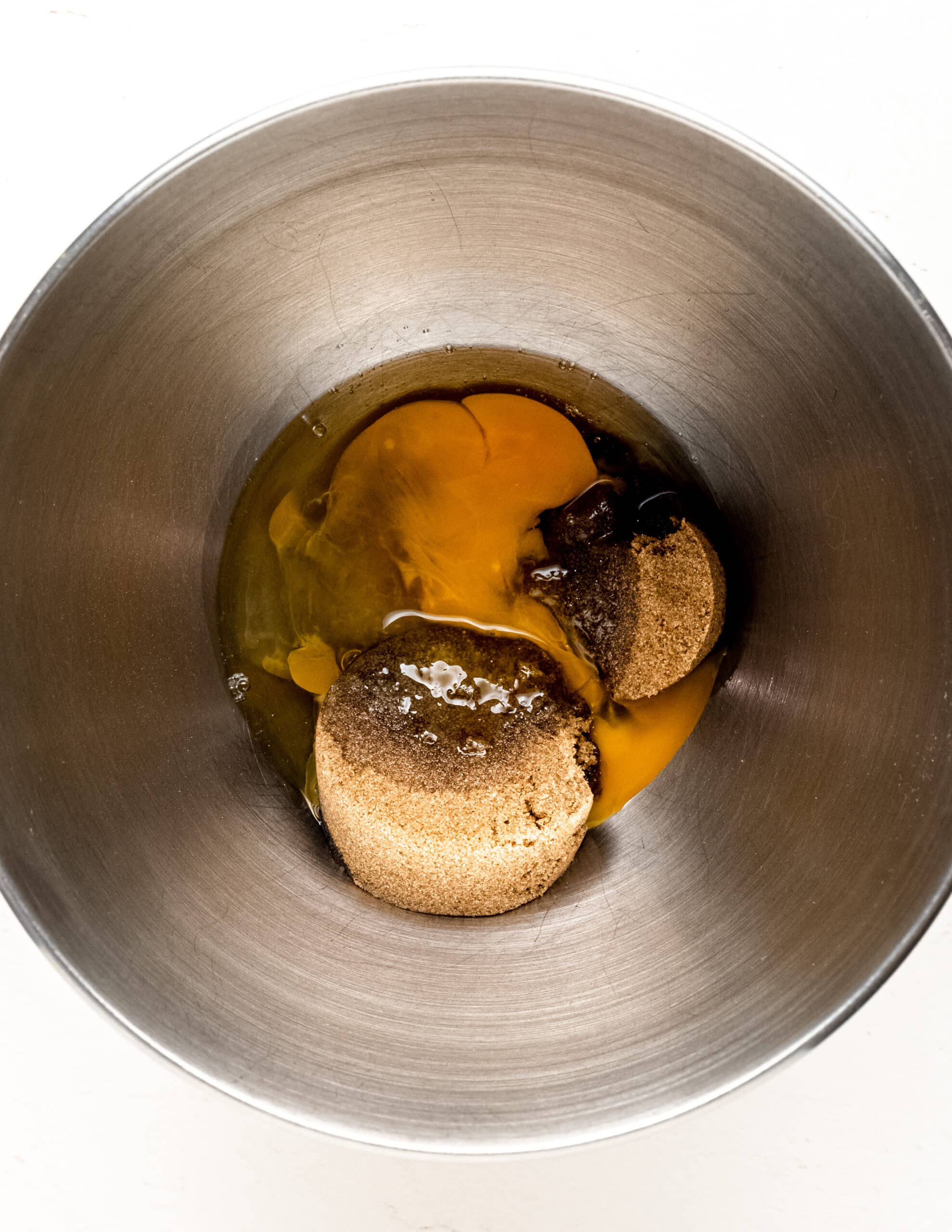 Overhead shot of two large eggs, dark brown sugar and white sugar in a silver mixing bowl.