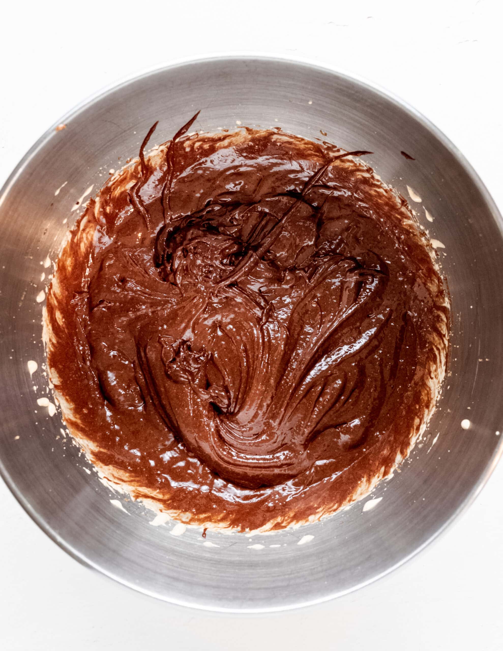 A silver mixing bowl with melted butter-chocolate mixture and egg-sugar mixture.